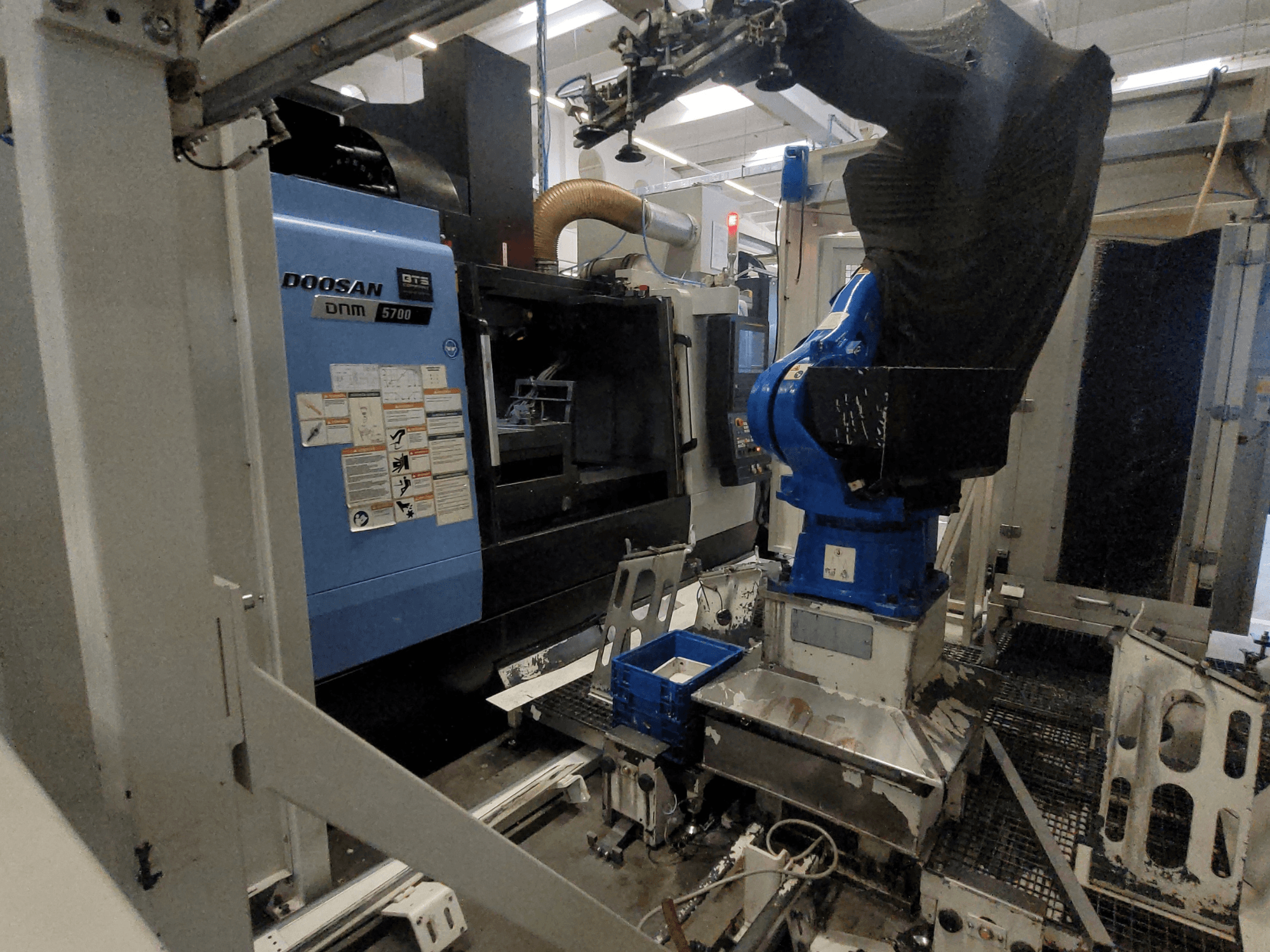 Вертикальний обробний центр DOOSAN DNM 5700 у заводському виконанні: на фото показано його вигляд спереду та інтеграцію з роботом-маніпулятором.