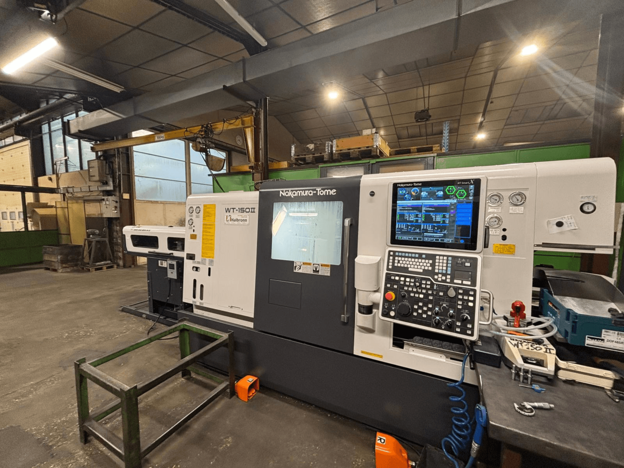 Верстат Nakamura-Tome WT-150II, вид спереду, з панеллю керування та інструментами на робочому столі в умовах майстерні.