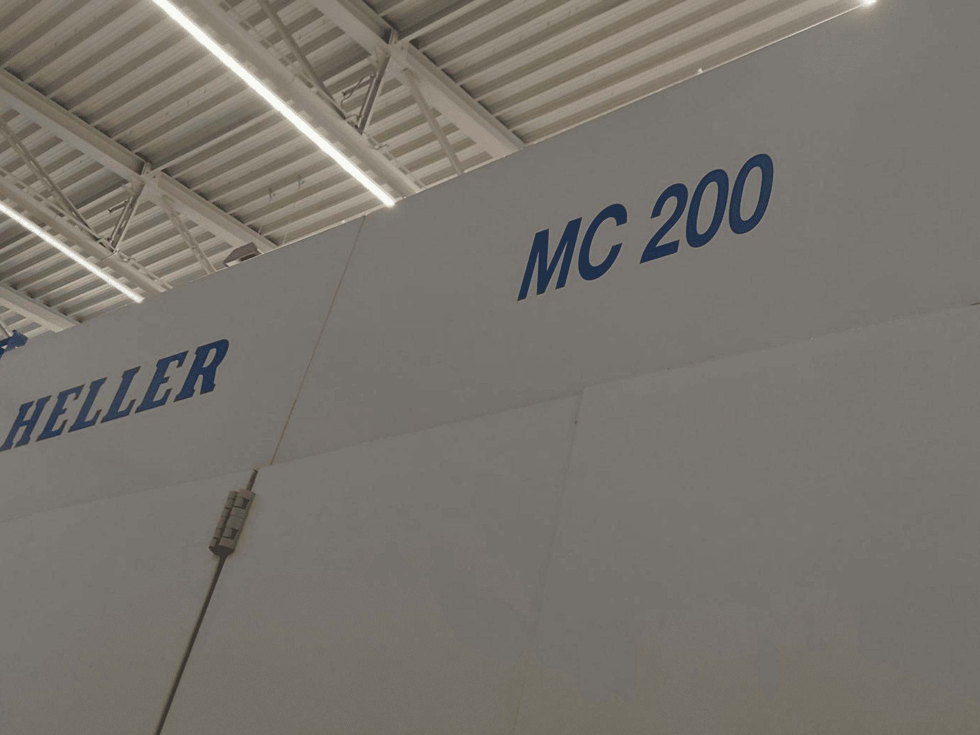 Горизонтальний обробний центр Heller MC 200, показаний збоку, з виділенням марки і моделі синім написом на білій поверхні.