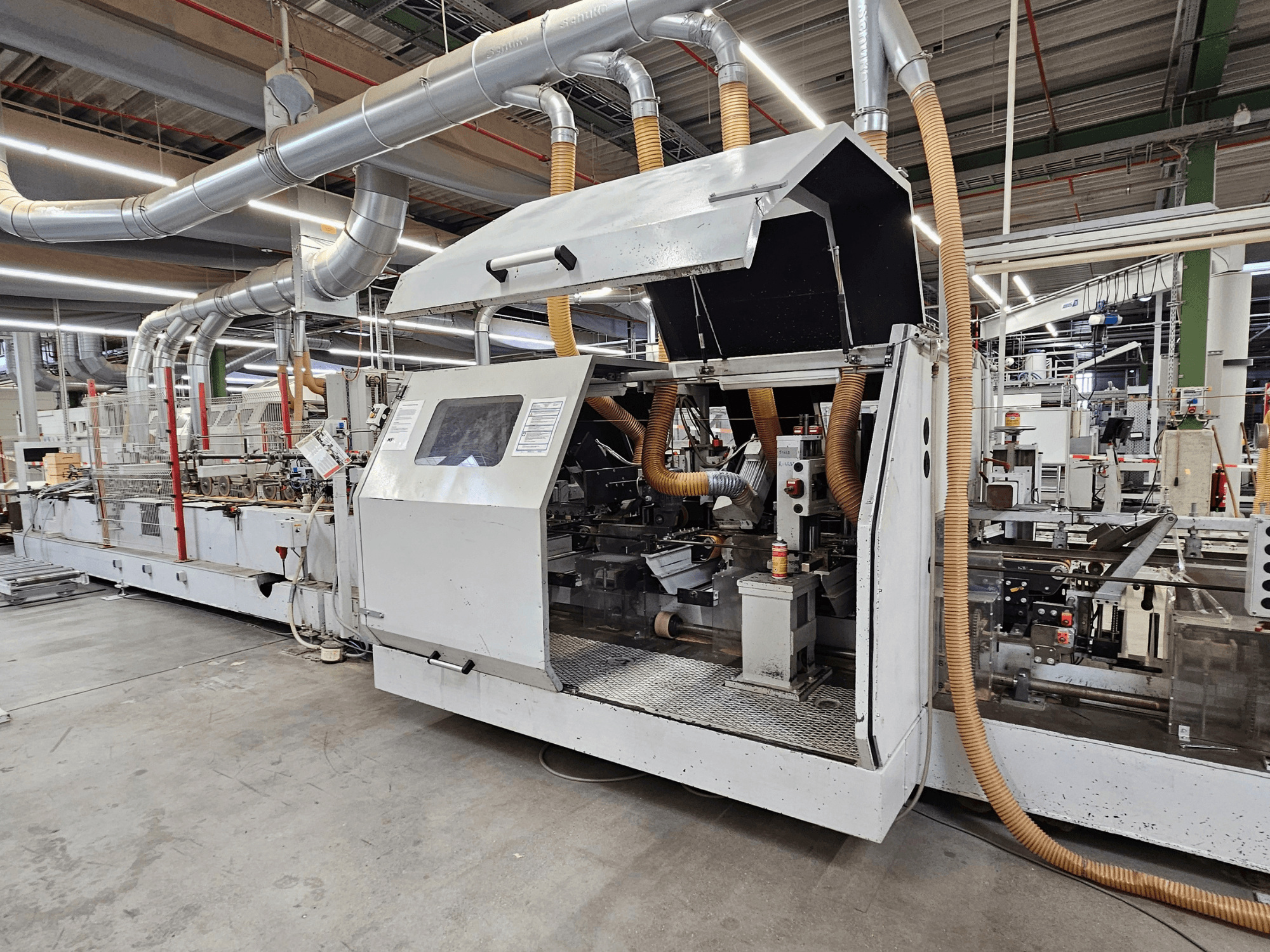 Кромкооблицювальний верстат HOMAG FG63 у заводських умовах, вид збоку з робочими компонентами та системою пиловідведення.