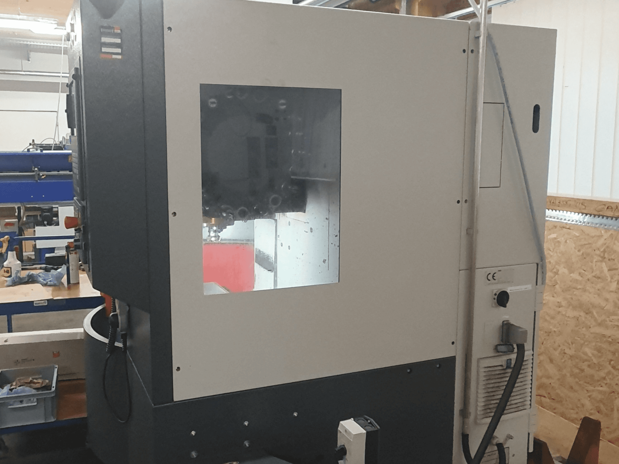 Вид збоку металообробного верстата з видимою панеллю керування, великим оглядовим вікном і складними внутрішніми компонентами.