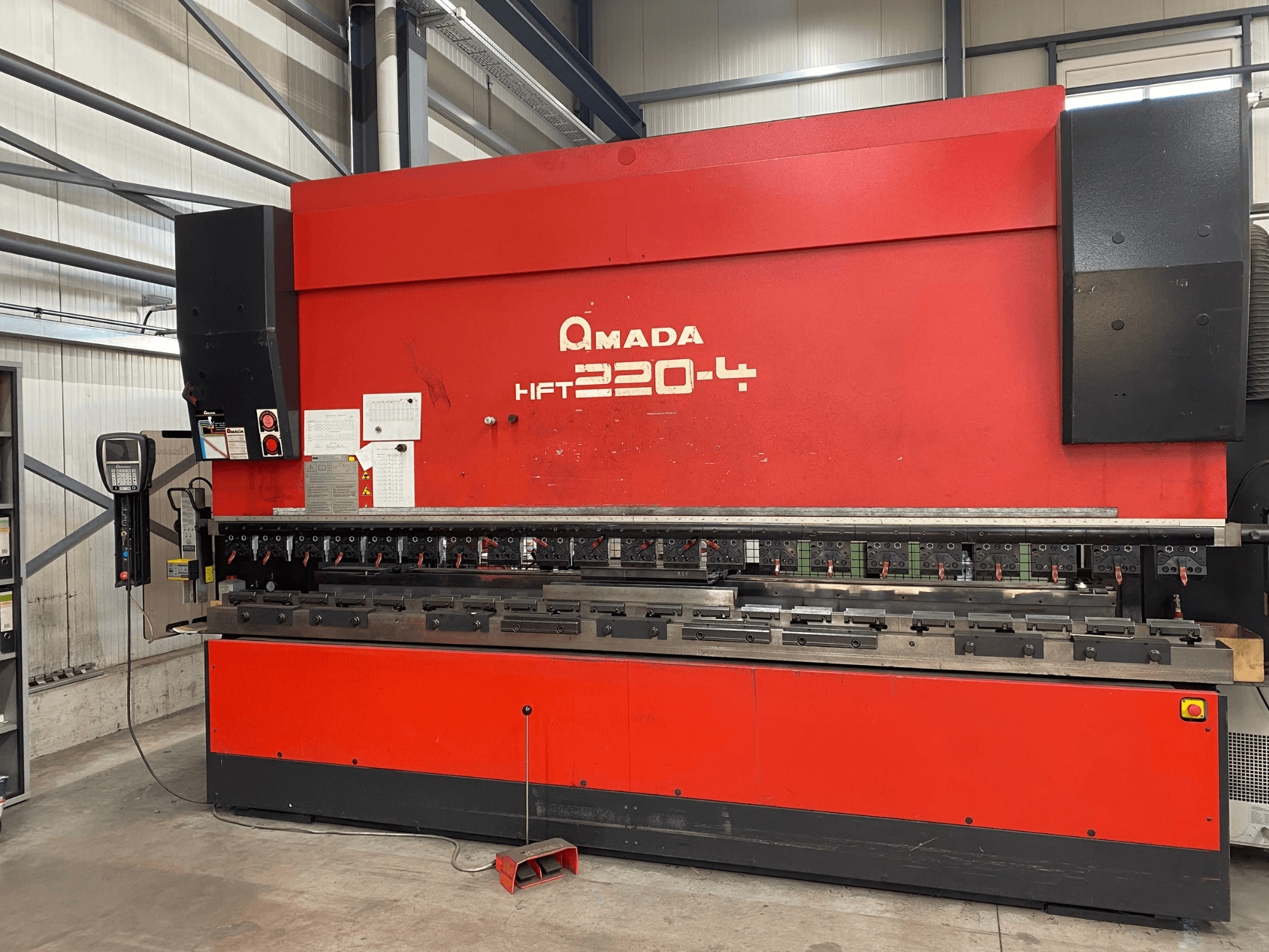 Червоний листозгинальний прес AMADA HFT 220-4 у заводській комплектації, вид спереду з панеллю керування та інструментами для згинання на робочій поверхні.