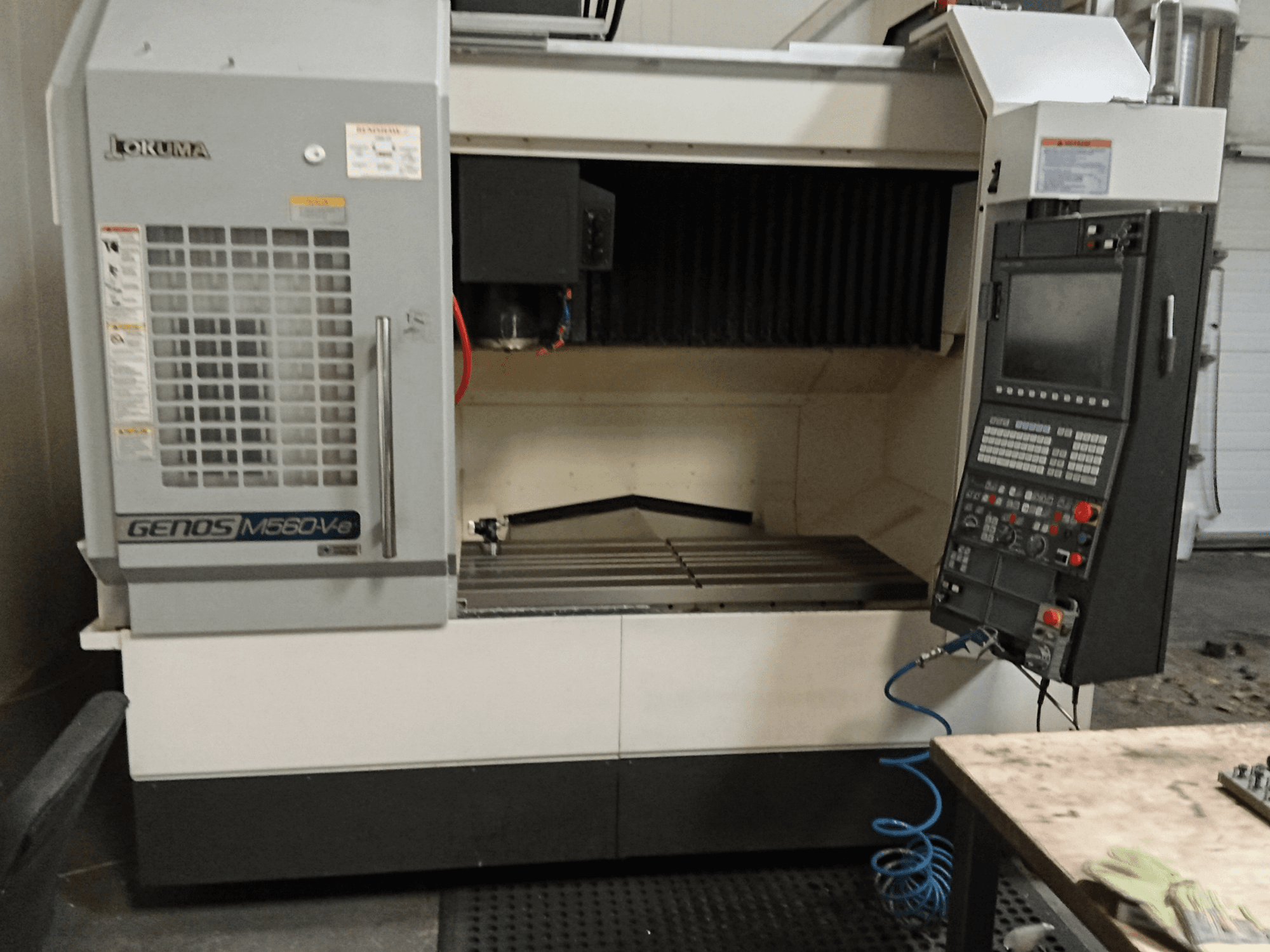 Okuma GENOS M560-V, вигляд спереду вертикального обробного центру з панеллю керування, інтерфейсом ЧПК та видимою зоною різання.
