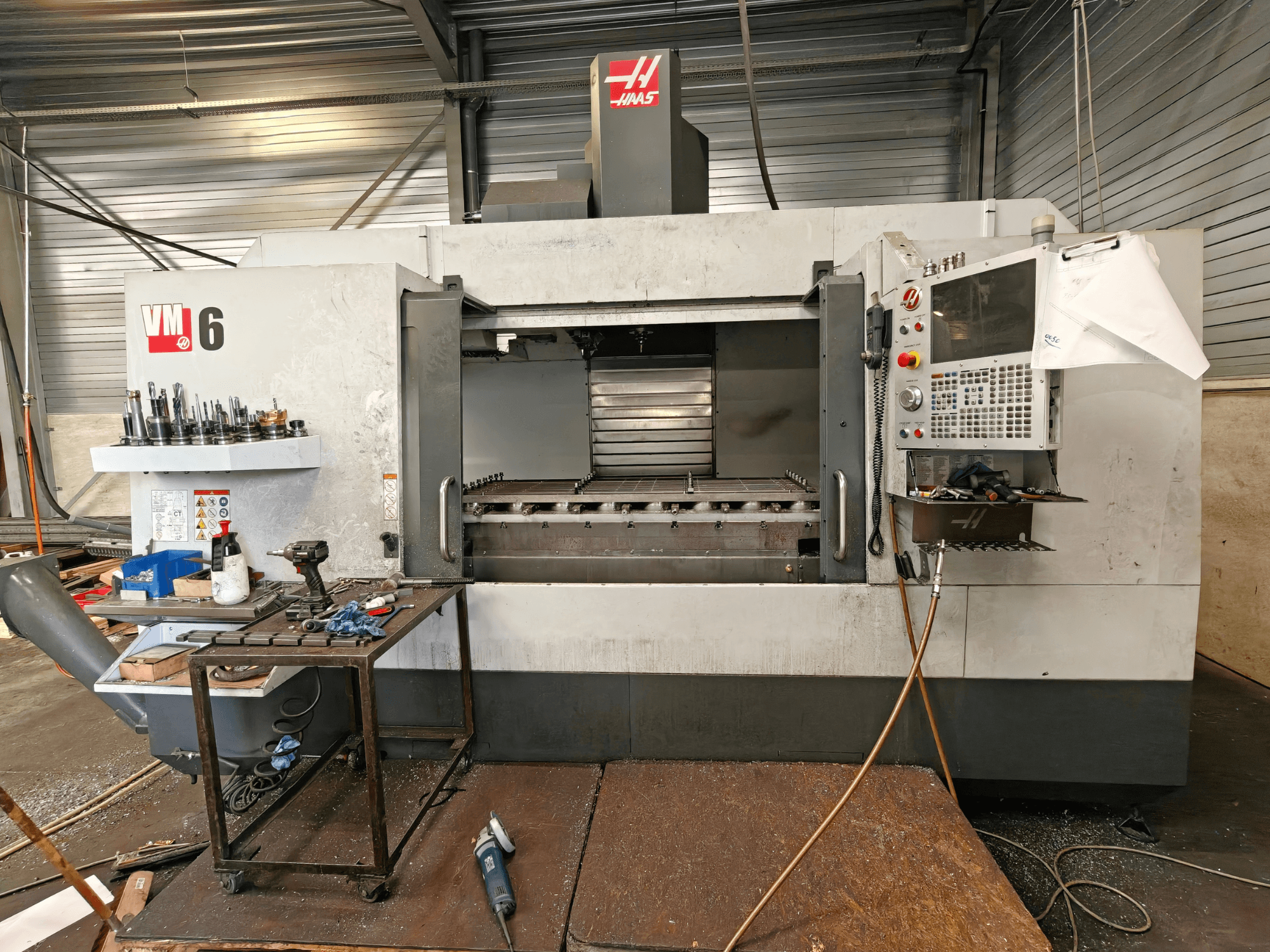 Вертикальний обробний центр Haas VM-6, вид спереду, на якому видно сховище інструментів, панель управління та сміття в робочій зоні.
