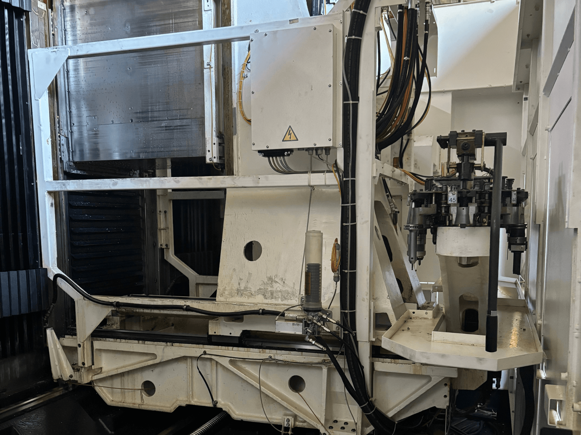 Вид збоку промислового верстата, що показує білий фрезерний верстат з ЧПУ з видимими інструментами, трубами та панеллю керування.