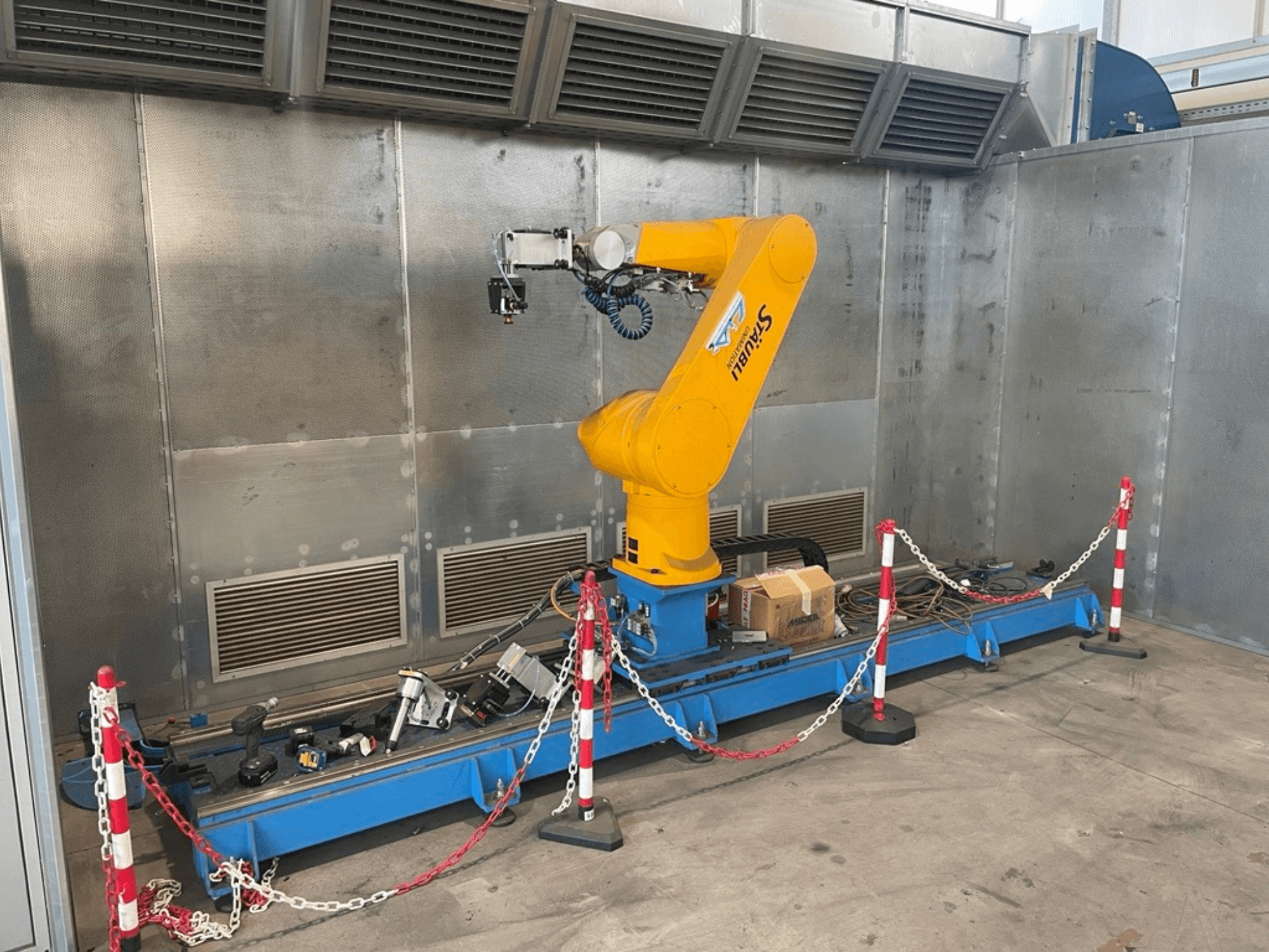 Робот-маніпулятор STAUBLI CS8C-RX160 в майстерні, вид збоку, з кабелями та різними інструментами на синій основі, оточеній захисними бар'єрами.