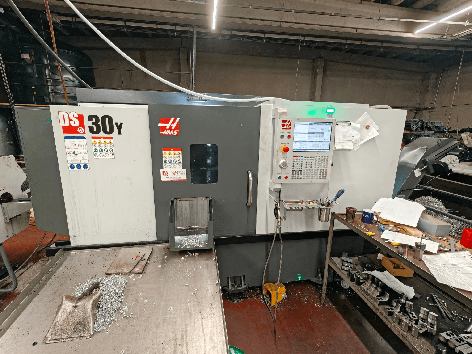 Горизонтальний токарний верстат HAAS DS30Y у цеху, вид спереду, на якому видно панель управління та металеву стружку на поверхні.