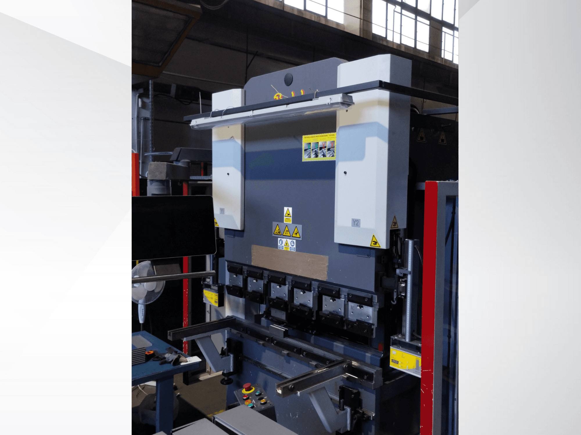 Листозгинальний верстат, вигляд спереду. Має видимі елементи керування, наклейки з техніки безпеки та кілька тримачів матриць для точного згинання.