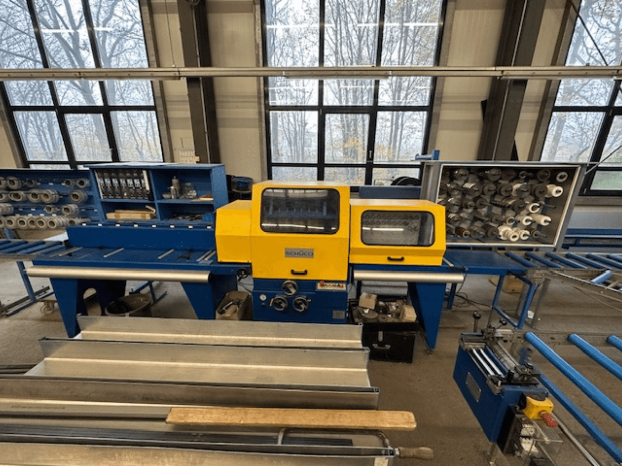 Вид спереду верстата SCHÜCO ISOMAT 4 з жовтою панеллю керування, кількома валками та відсіком для зберігання.