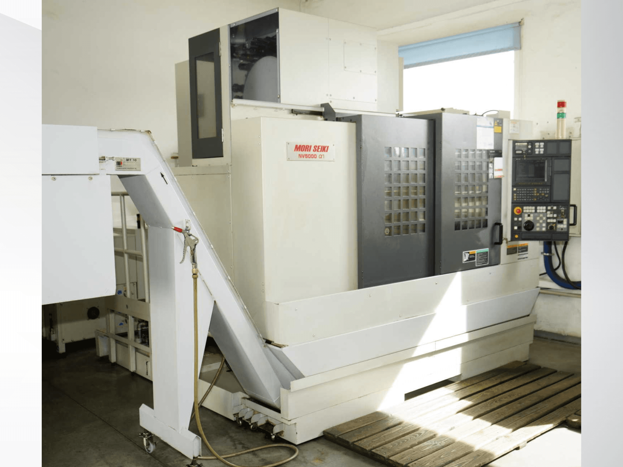 Вертикальний обробний центр MORI SEIKI NV 5000 alpha1 у фронтальному ракурсі, на якому видно панель керування, засоби безпеки та зону завантаження.