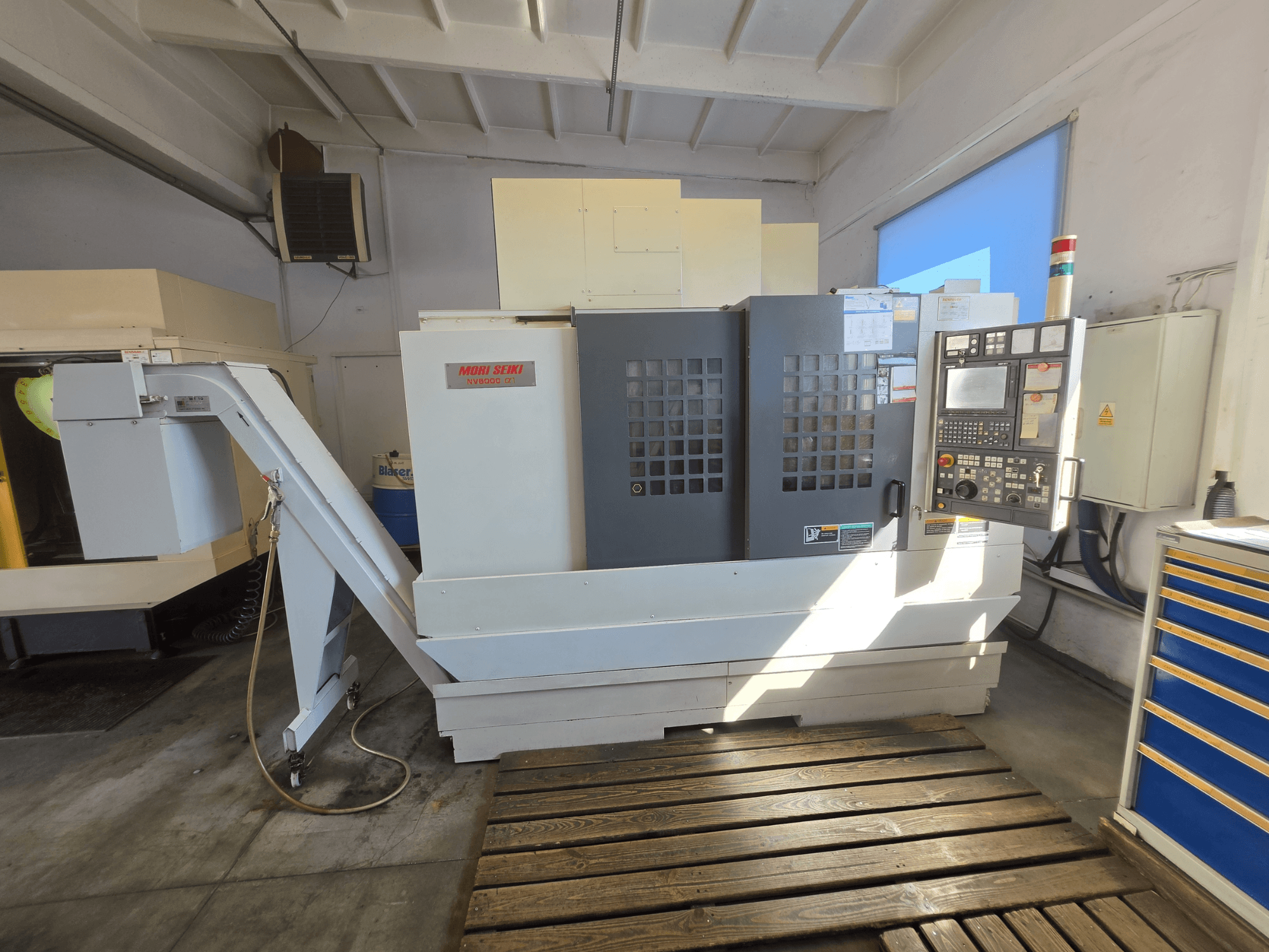 Вертикальний обробний центр MORI SEIKI NV 5000 alpha1, вид спереду, на якому видно панель керування та особливості верстата в умовах цеху.