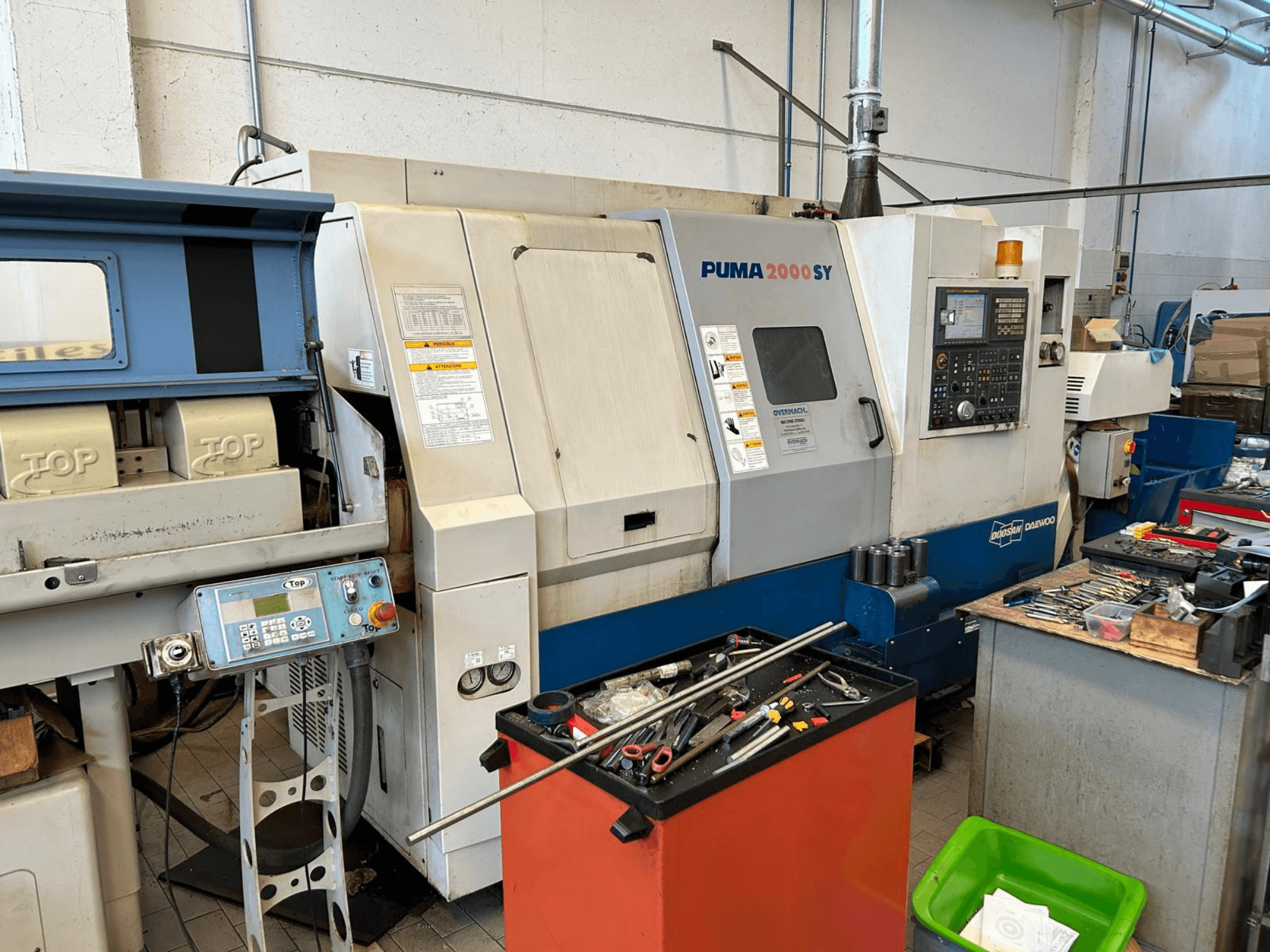 Горизонтальний токарний верстат DOOSAN PUMA 2000SY у цеху, вид збоку, на якому видно панель управління та інструменти поруч.