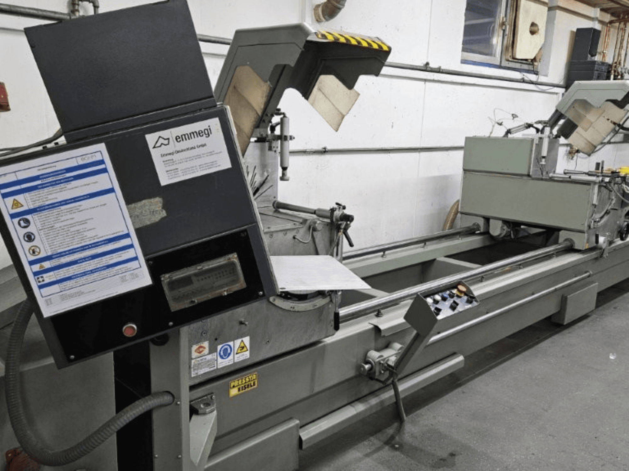 Промисловий розкрійний верстат Emmegi, вид спереду, панель управління, етикетки безпеки та робочі компоненти.