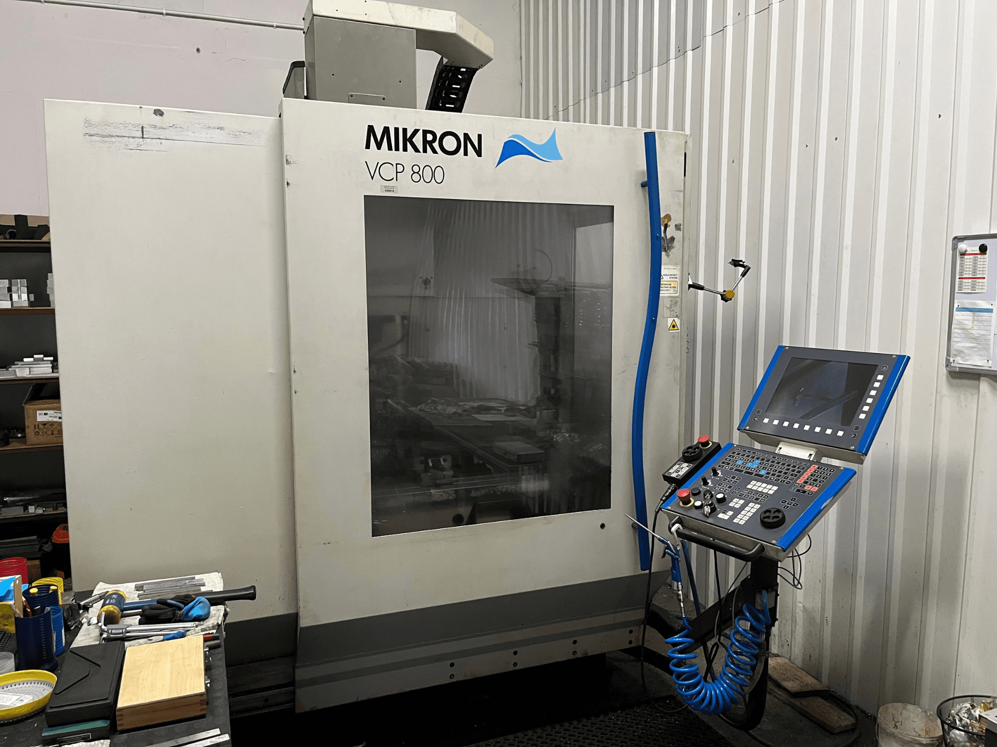 Вертикальний обробний центр MIKRON VCP 800, вид спереду, з панеллю керування та інструментами на верстаті на передньому плані.