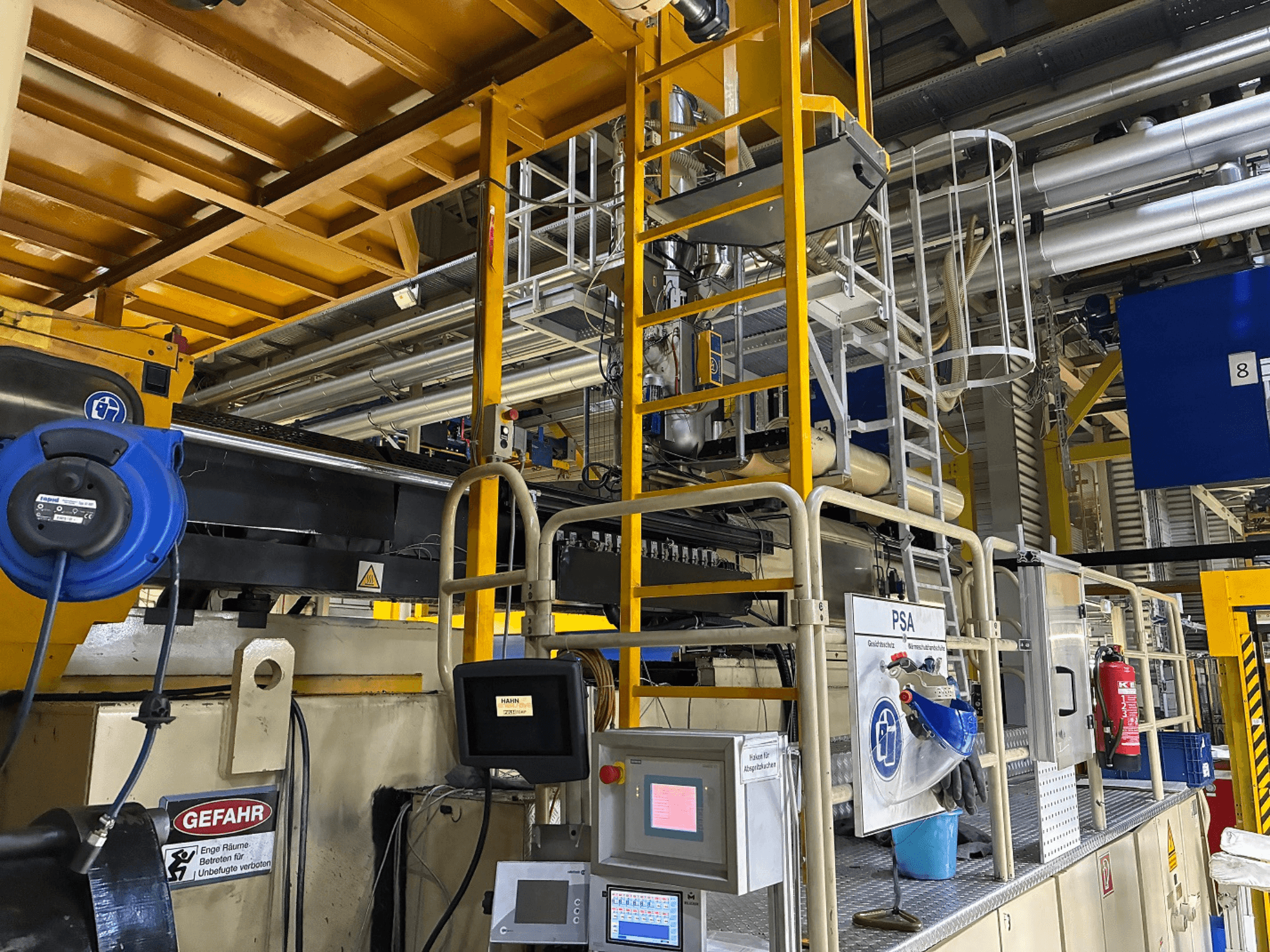 Панель управління промисловим обладнанням з синім захисним обладнанням і жовтими риштуваннями, вид збоку з трубами і попереджувальними знаками.