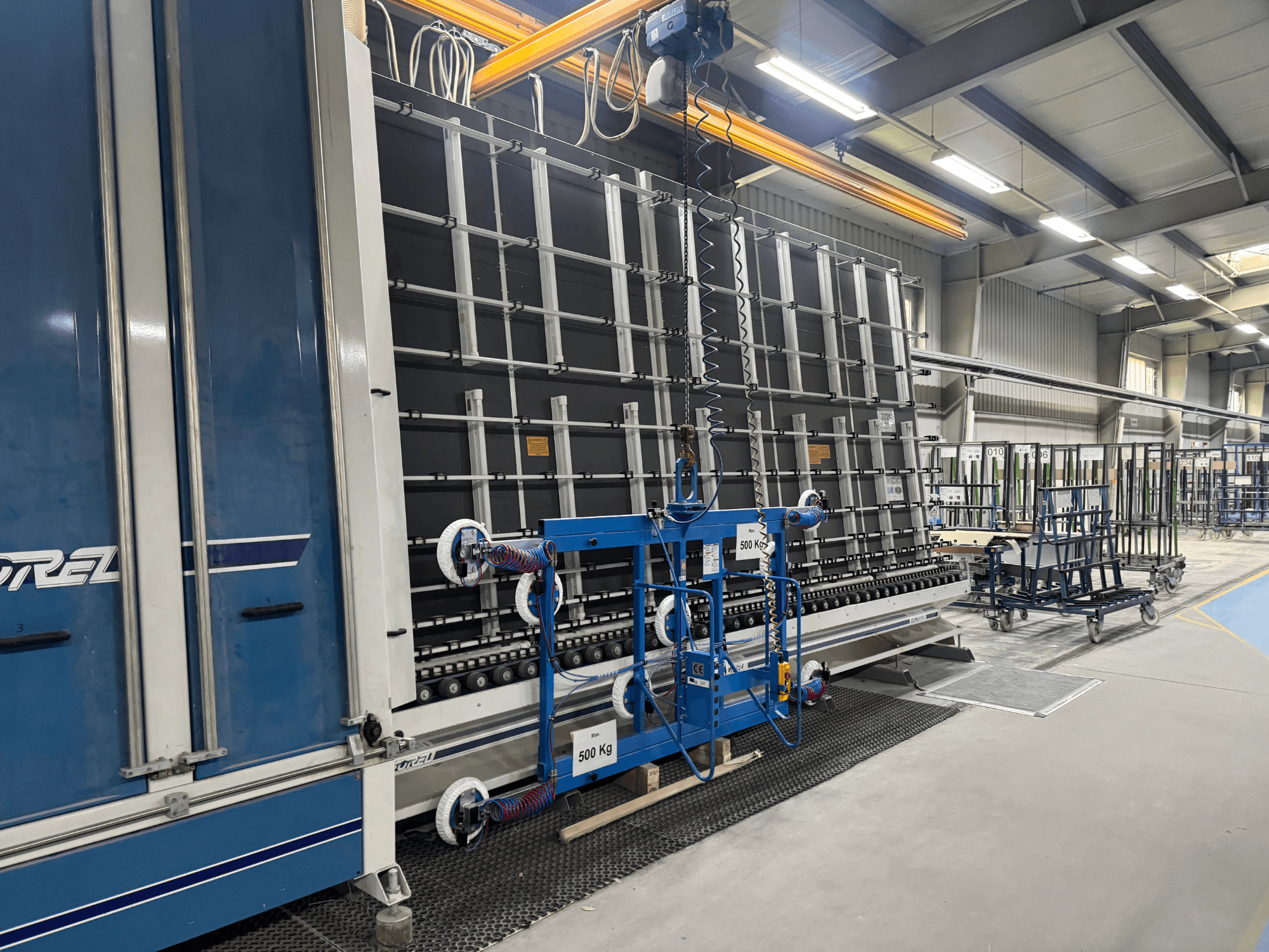 Промислове обладнання Drel з великою рамою і підйомним механізмом, показане збоку в заводських умовах.