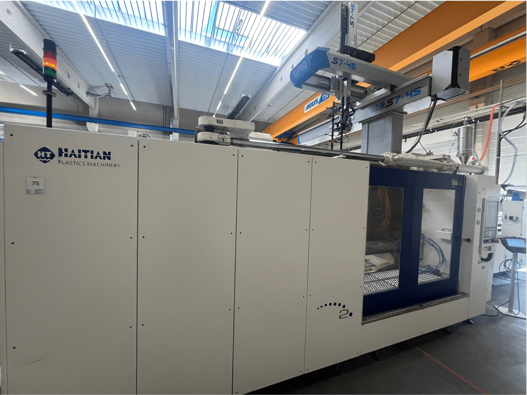 Термопластавтомат Haitian S7-45 у вигляді збоку з панеллю керування та світловим індикатором безпеки. Біло-блакитний дизайн.