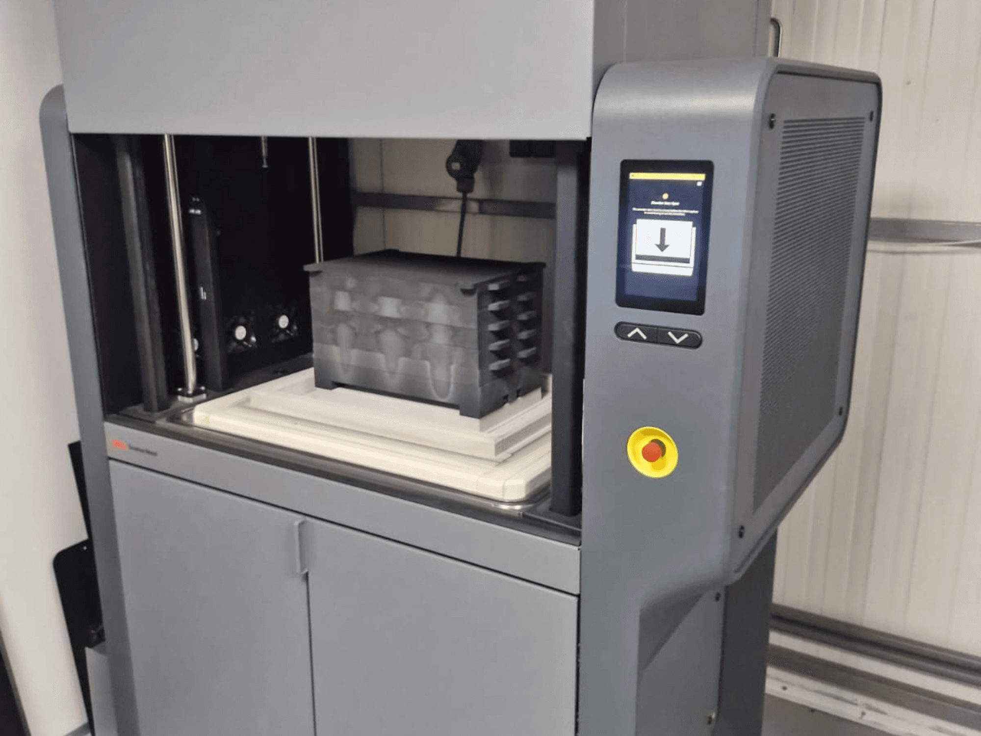 3D-принтер Metal Studio 2 від компанії Desktop Metal, вид спереду з панеллю керування та робочим столом з чорним контейнером.