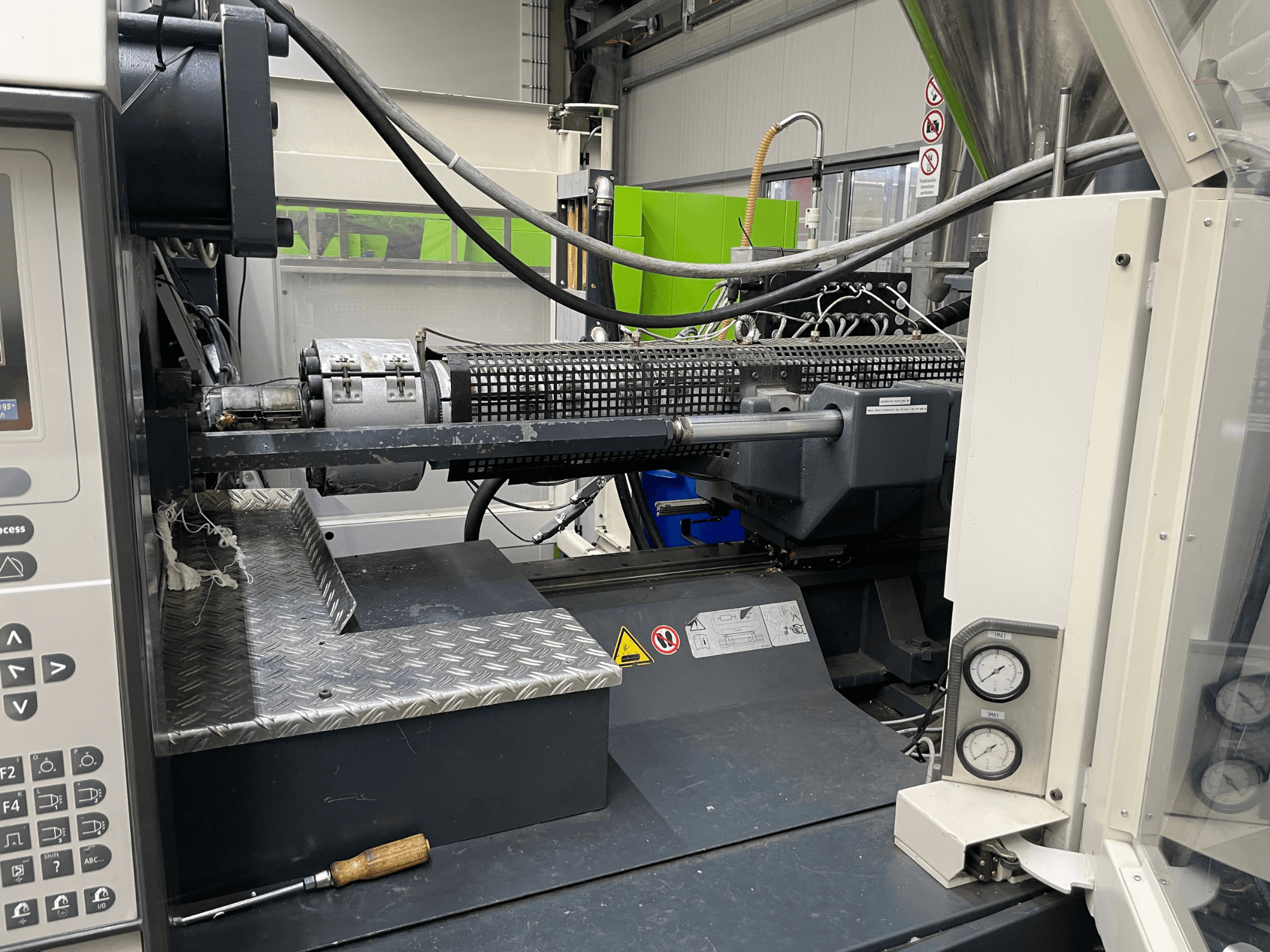 Вид збоку термопластавтомата з панеллю керування, екструдером і манометрами, ідеально підходить для виконання виробничих завдань.