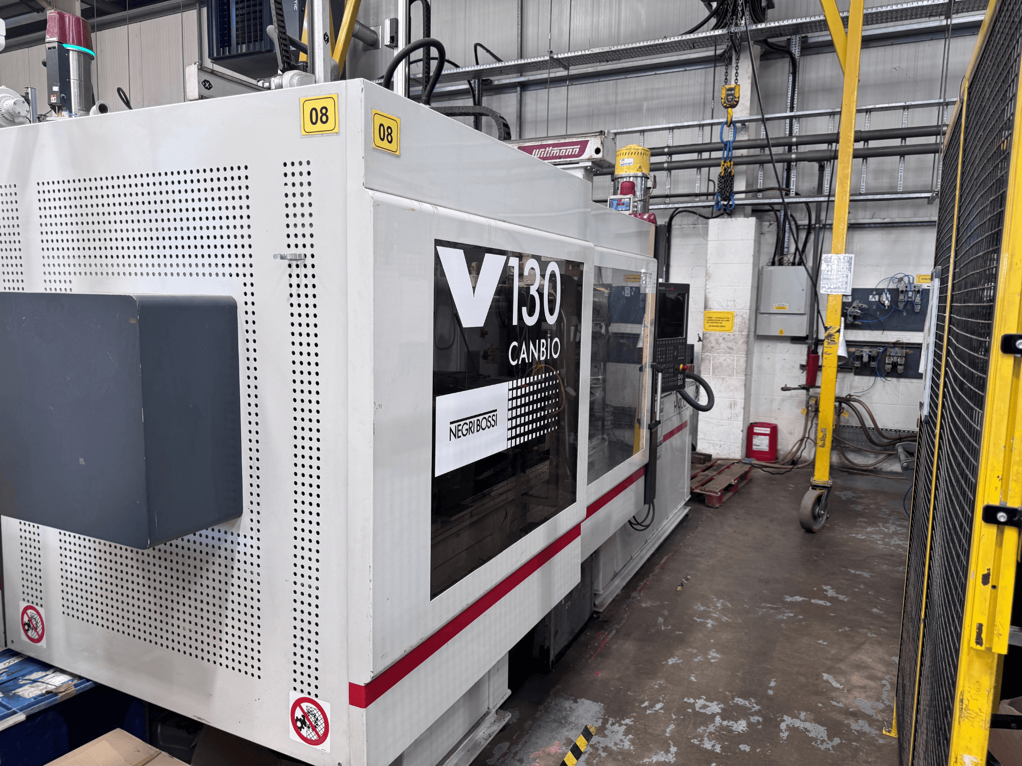 Гідравлічна термопластавтомат Negri Bossi 1300H-400, вид збоку, з панеллю управління та знаками безпеки.