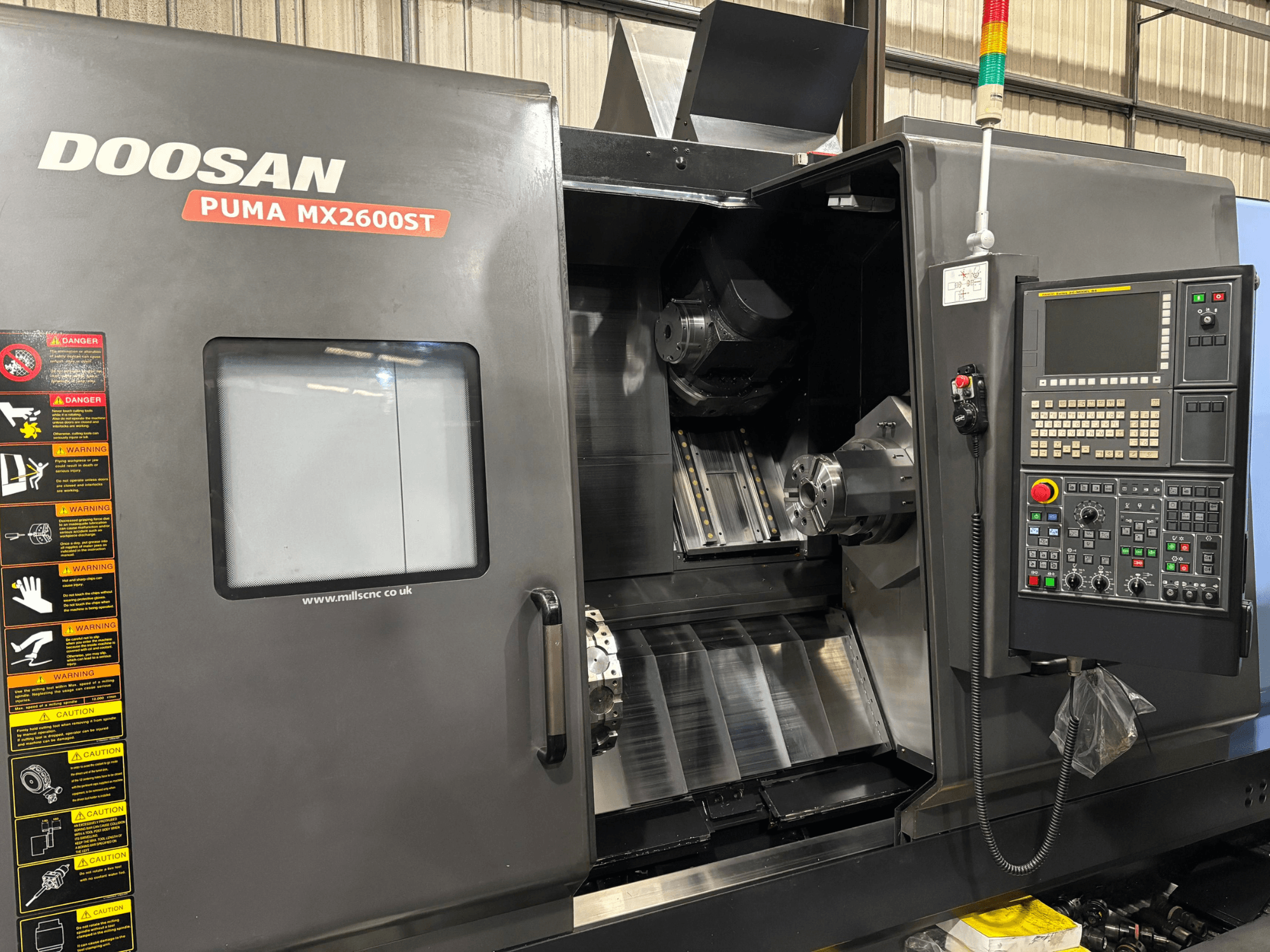 Токарний верстат з ЧПК Doosan PUMA MX2600ST, вид спереду, з панеллю керування, шпинделем і зоною обробки з видимими попередженнями про безпеку.