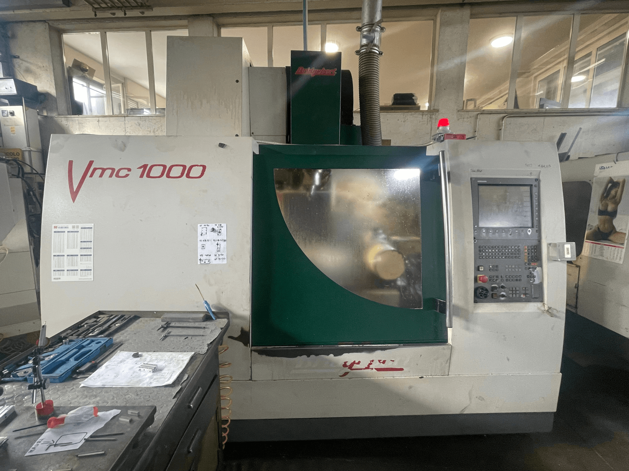 Вертикальний обробний центр Bridgeport VMC 1000/30, вид спереду, на якому видно панель управління та основний корпус, а поруч — інструменти.