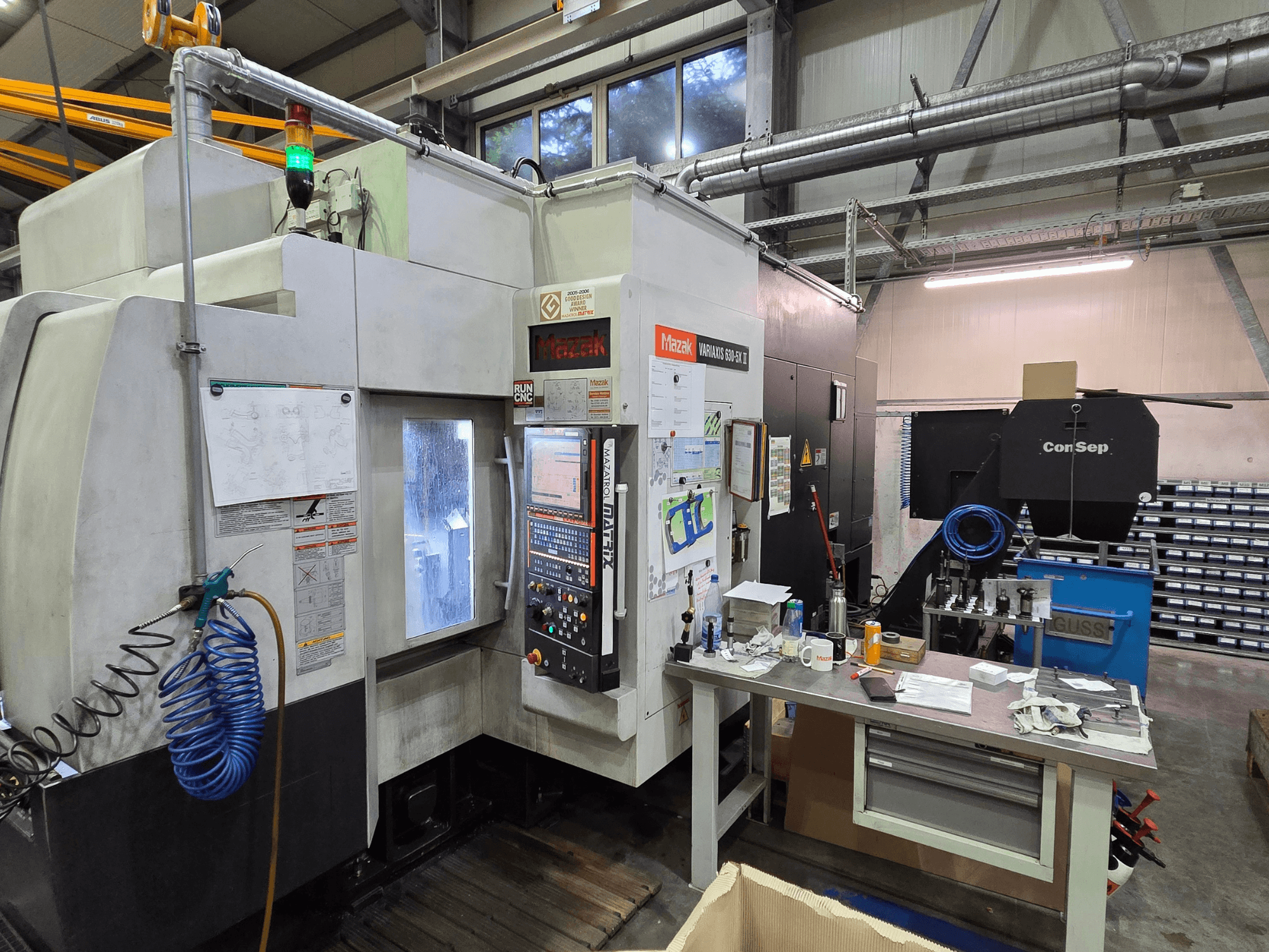 Верстат з ЧПК Mazak Variaxis 630-5X в майстерні, вид спереду з панеллю керування, шлангом та аксесуарами на боковому столі.