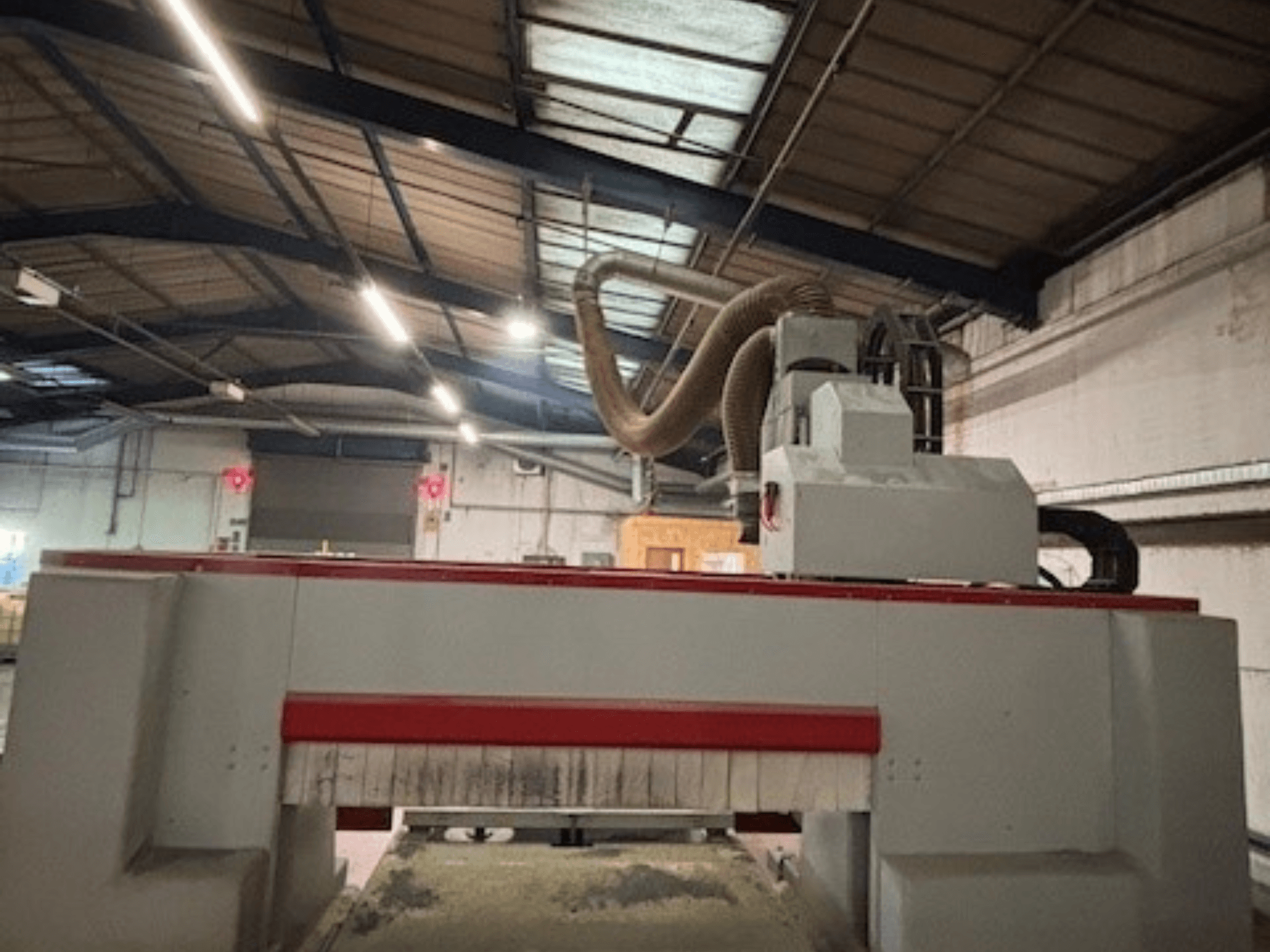 Фрезерний верстат з ЧПУ в майстерні, вид збоку, що підкреслює червоно-сірий дизайн, встановлена система відсмоктування пилу.