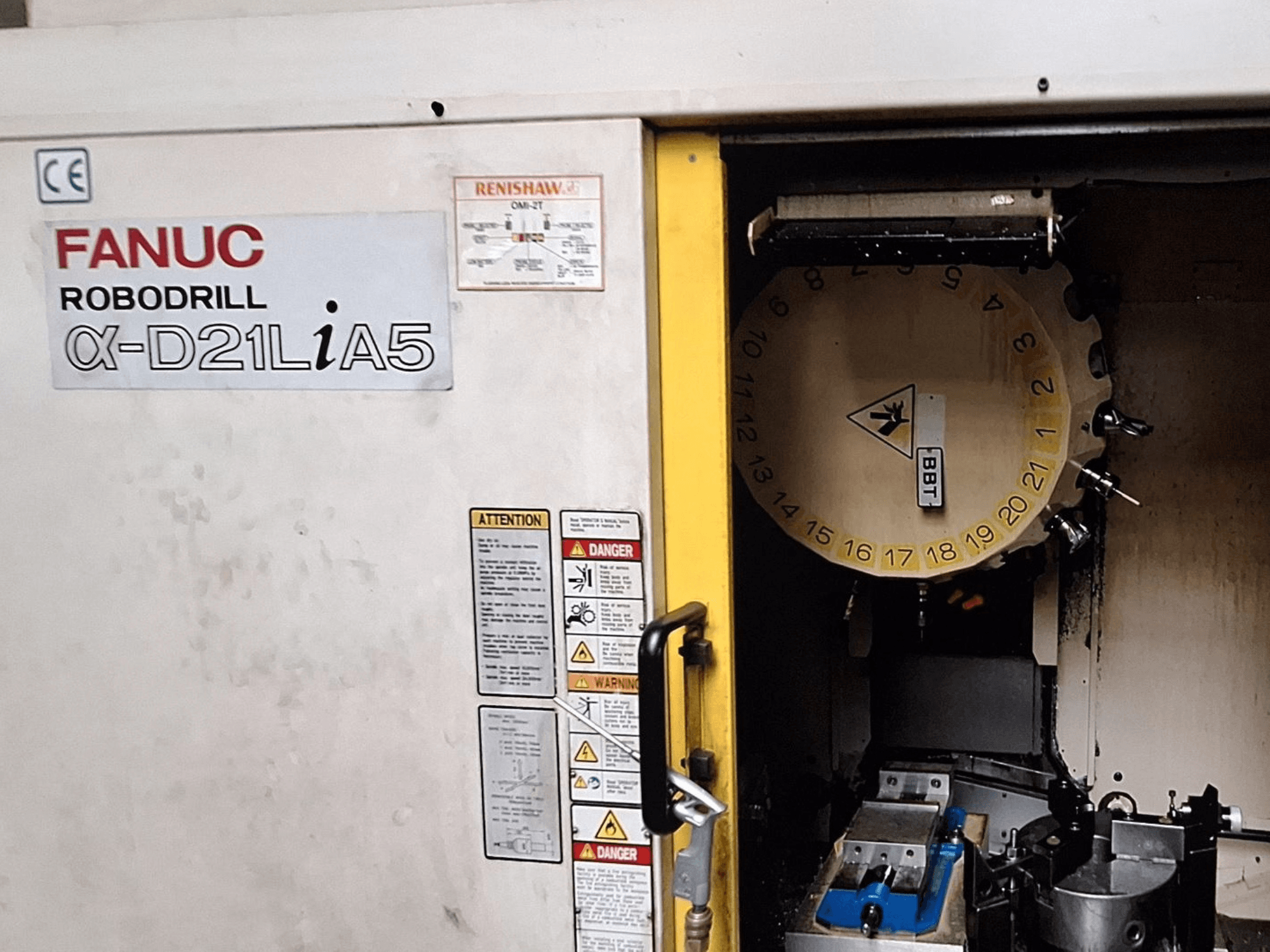 FANUC Robodrill α-D21LiA5, вигляд спереду. Показано карусель інструментів і зону обробки із затискачами та попередженнями на дверцятах.