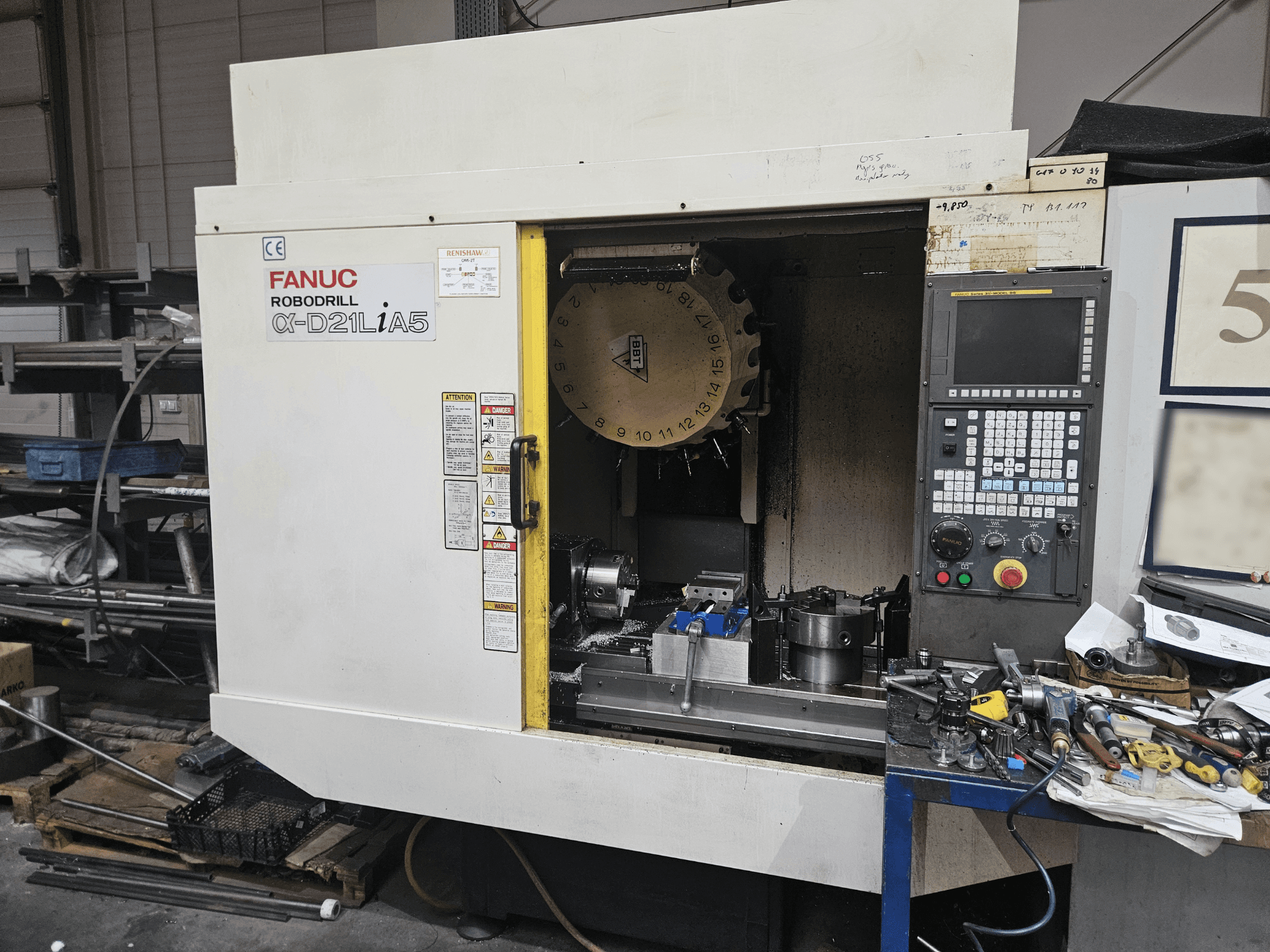 FANUC Robodrill α-D21LiA5, вид спереду з тримачем інструменту та панеллю керування в оточенні інструментів та обладнання в майстерні.