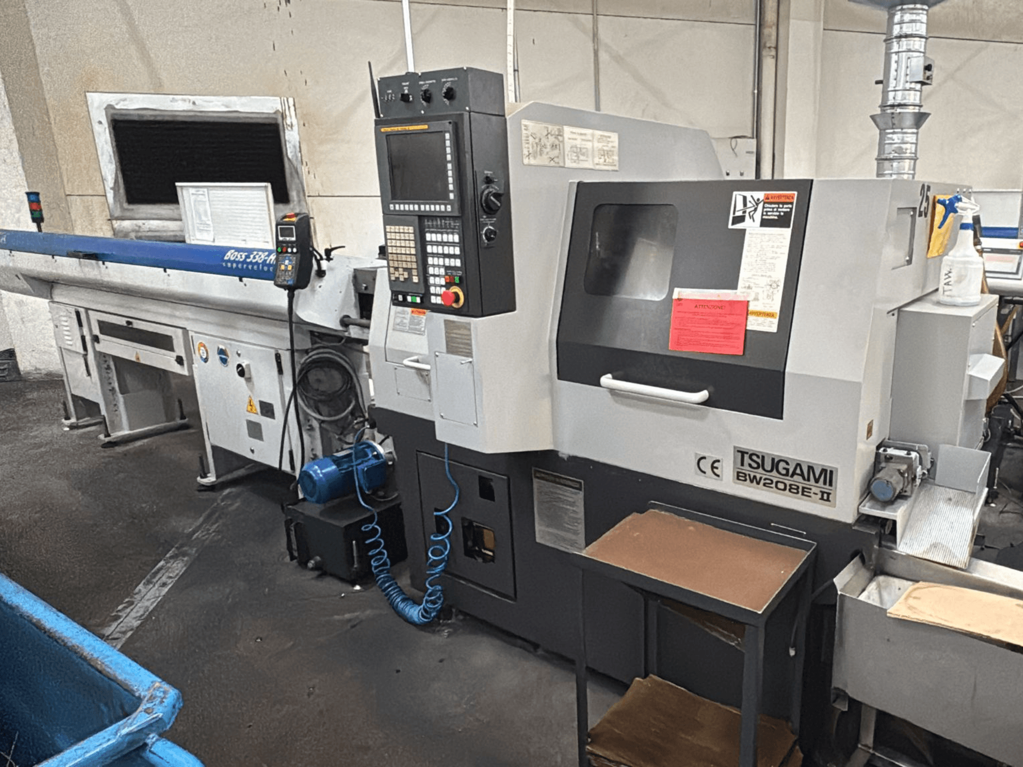 Верстат з ЧПК Tsugami BW208E-II в майстерні, показаний спереду, з панеллю керування та етикетками безпеки.