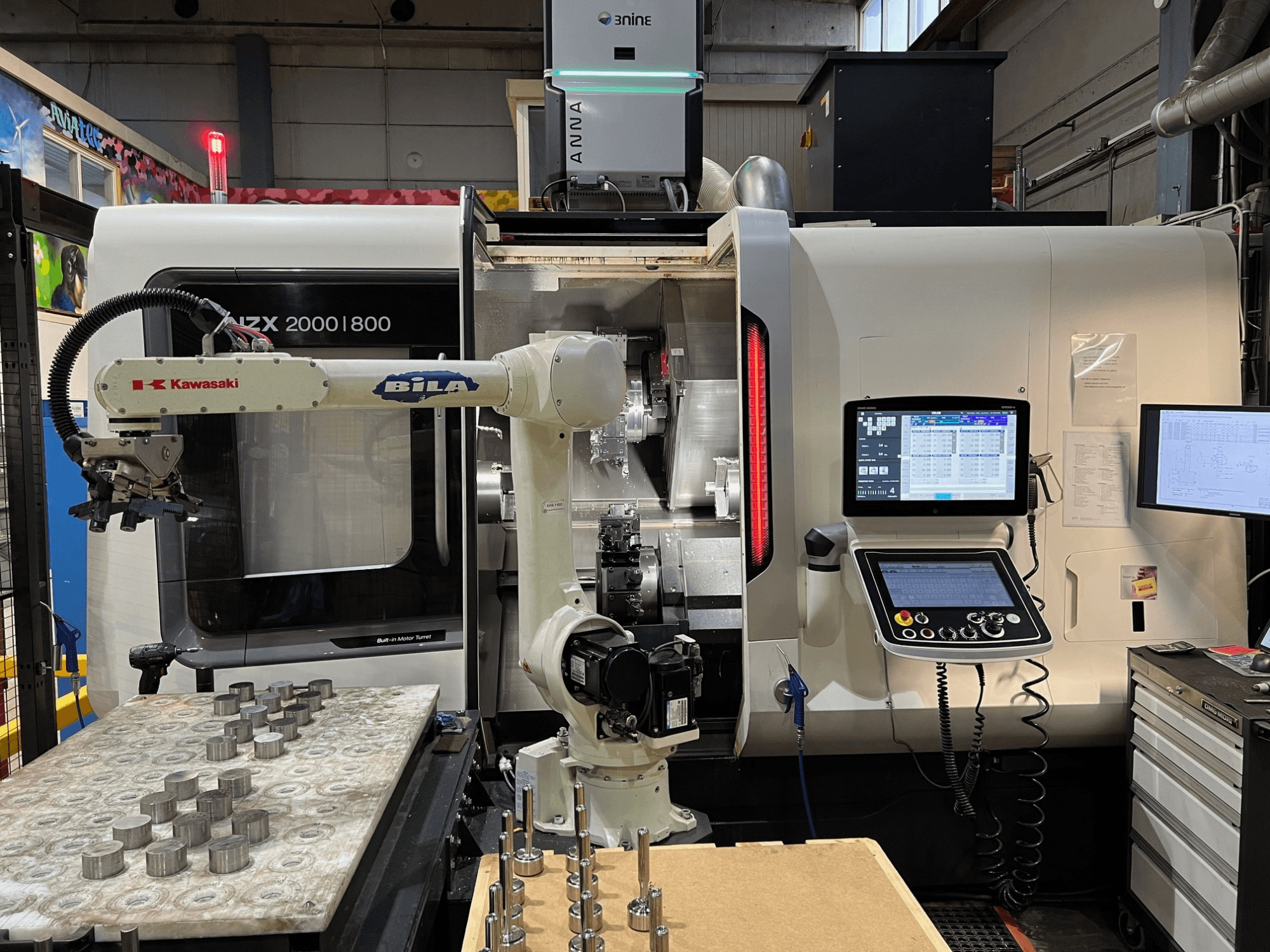 Горизонтальний токарний верстат DMG MORI NZX 2000/800SY у цеху; на фото видно робот-маніпулятор Kawasaki та пульт управління.
