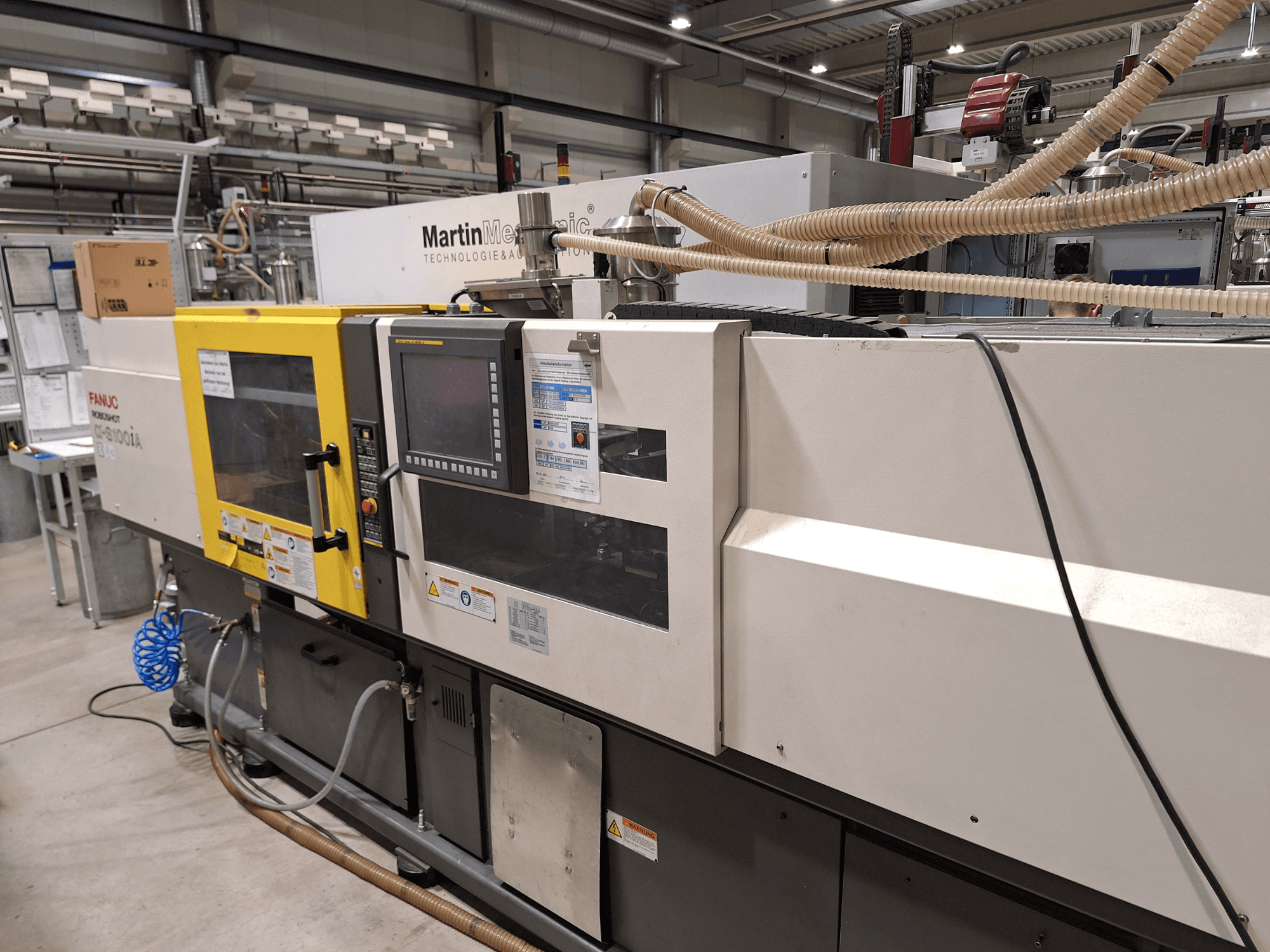 Електричний термопластавтомат FANUC Roboshot S100iA, вид збоку, оснащений сенсорним екраном і етикетками безпеки.