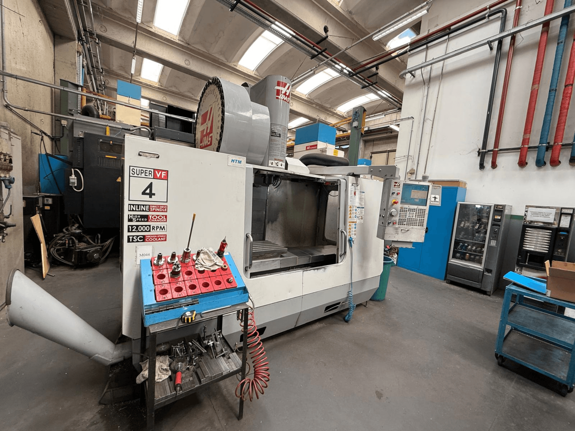 Фрезерний верстат HAAS Super VF 4 з ЧПК з панеллю керування, шпинделем 12 000 об/хв та інструментами на синьому стелажі, вид збоку.
