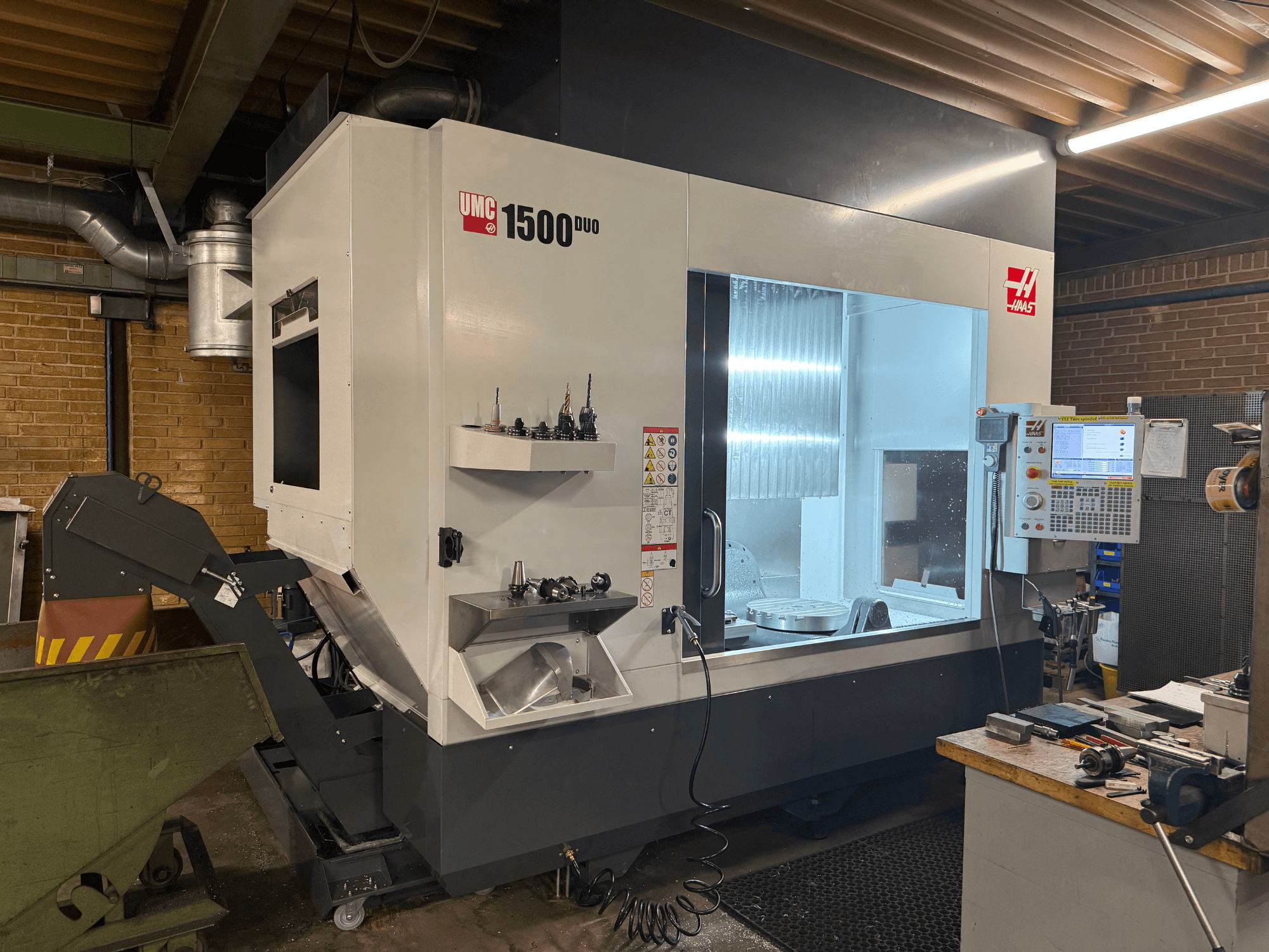 Верстат з ЧПК Haas UMC 1500DUO, вид спереду, має велике вікно, панель керування та тримачі для інструментів на полиці.