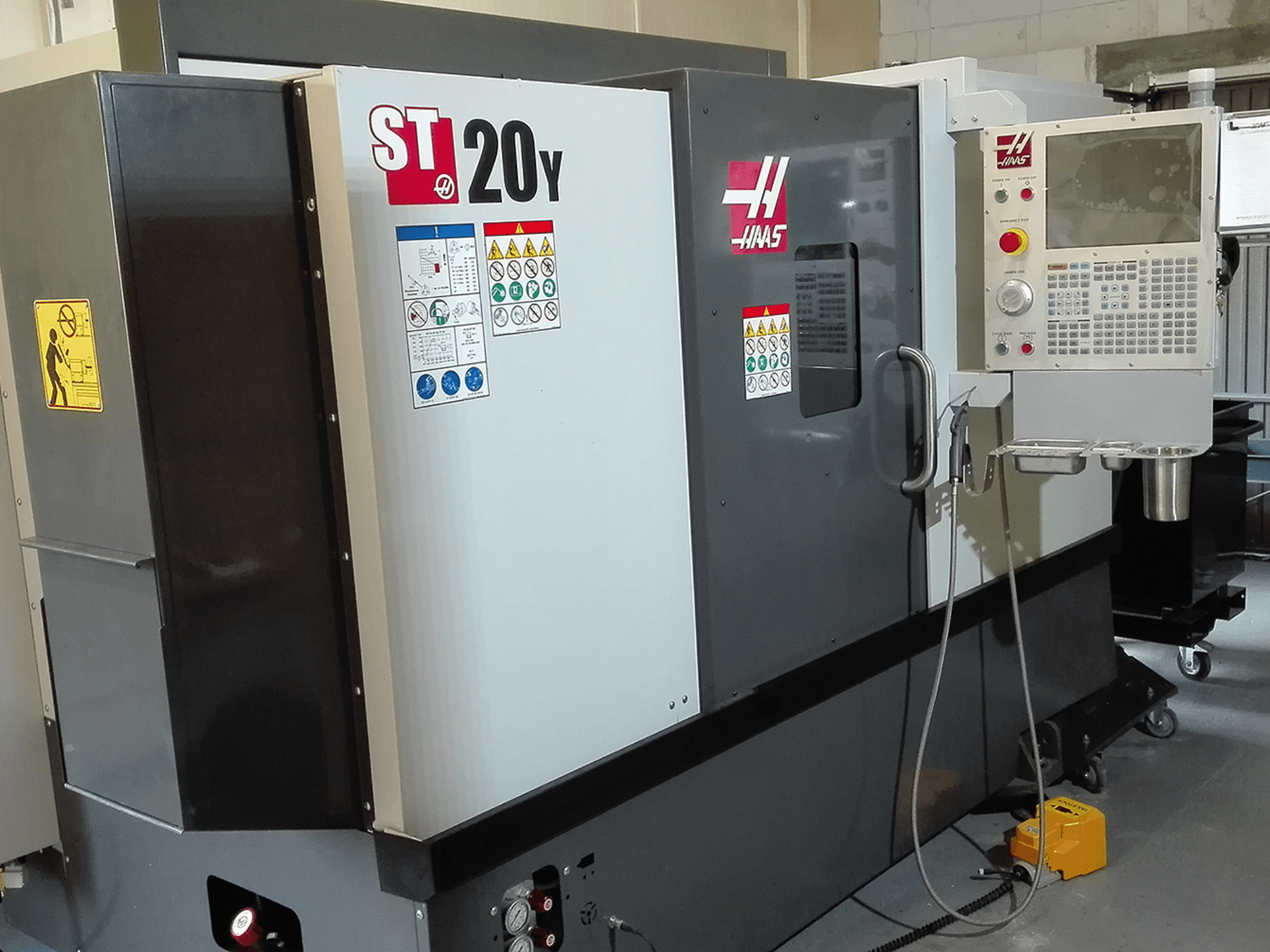 Токарний верстат з ЧПК Haas ST20Y спереду, з панеллю керування, знаками безпеки та системою охолодження.