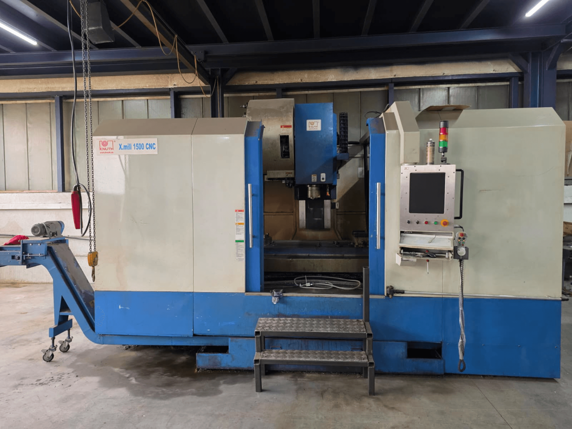 Вертикальний обробний центр KNUTH X-MILL 1500 з ЧПУ, вид збоку; на зображенні показано панель керування, сходи та вихідний конвеєр.