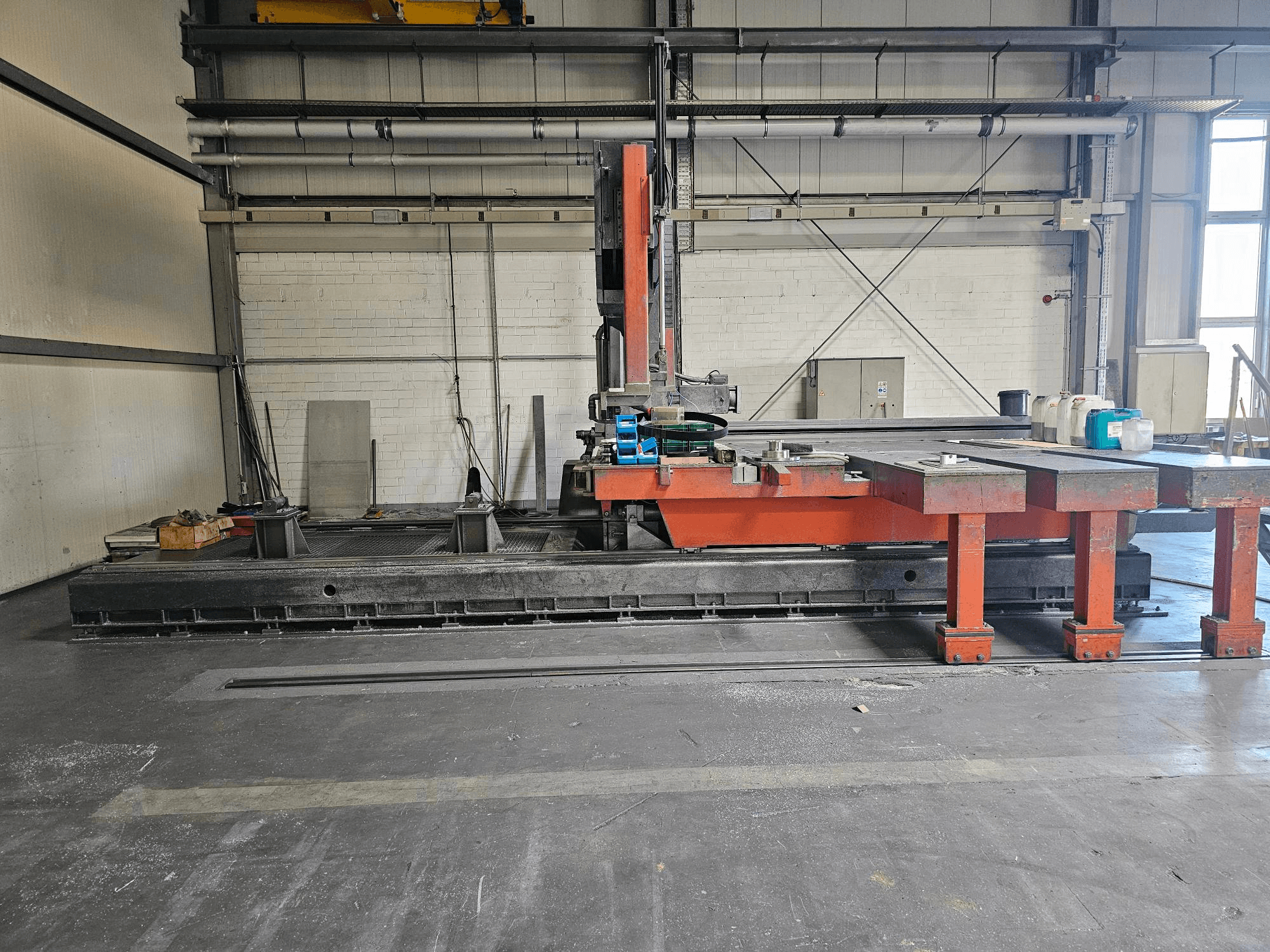 Промисловий розкрійний верстат у відкритій майстерні, оранжево-чорний з великим столом; вид збоку з аксесуарами та робочим простором.