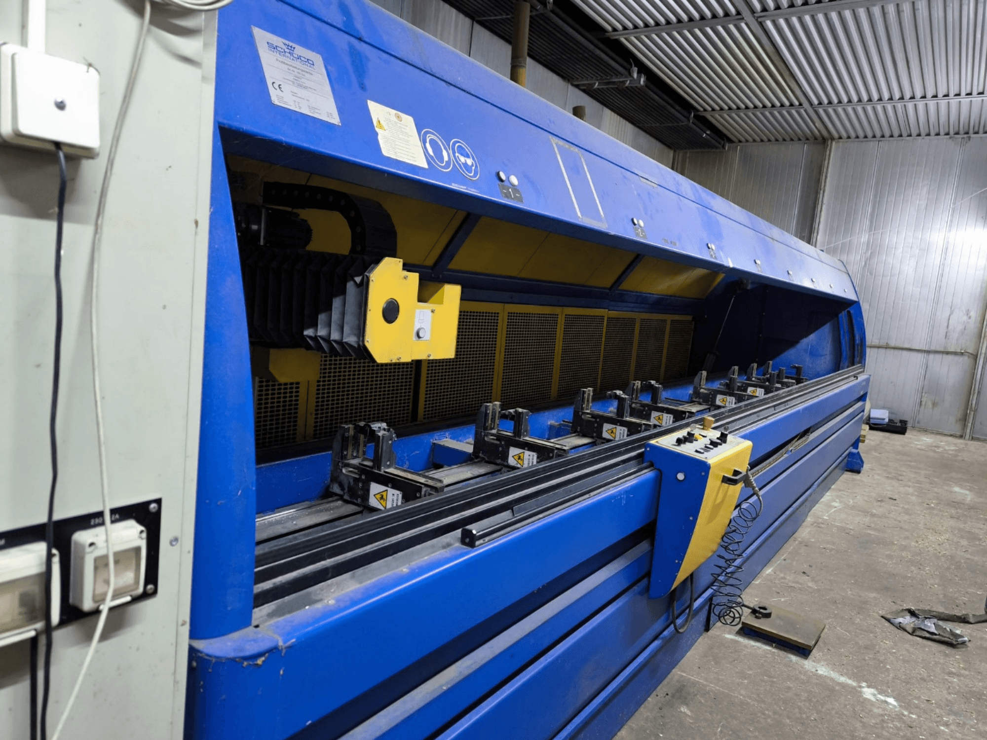 Промисловий розкрійний верстат Schneider синього кольору, вид збоку, видно панель керування, ремені та кілька затискних станцій.