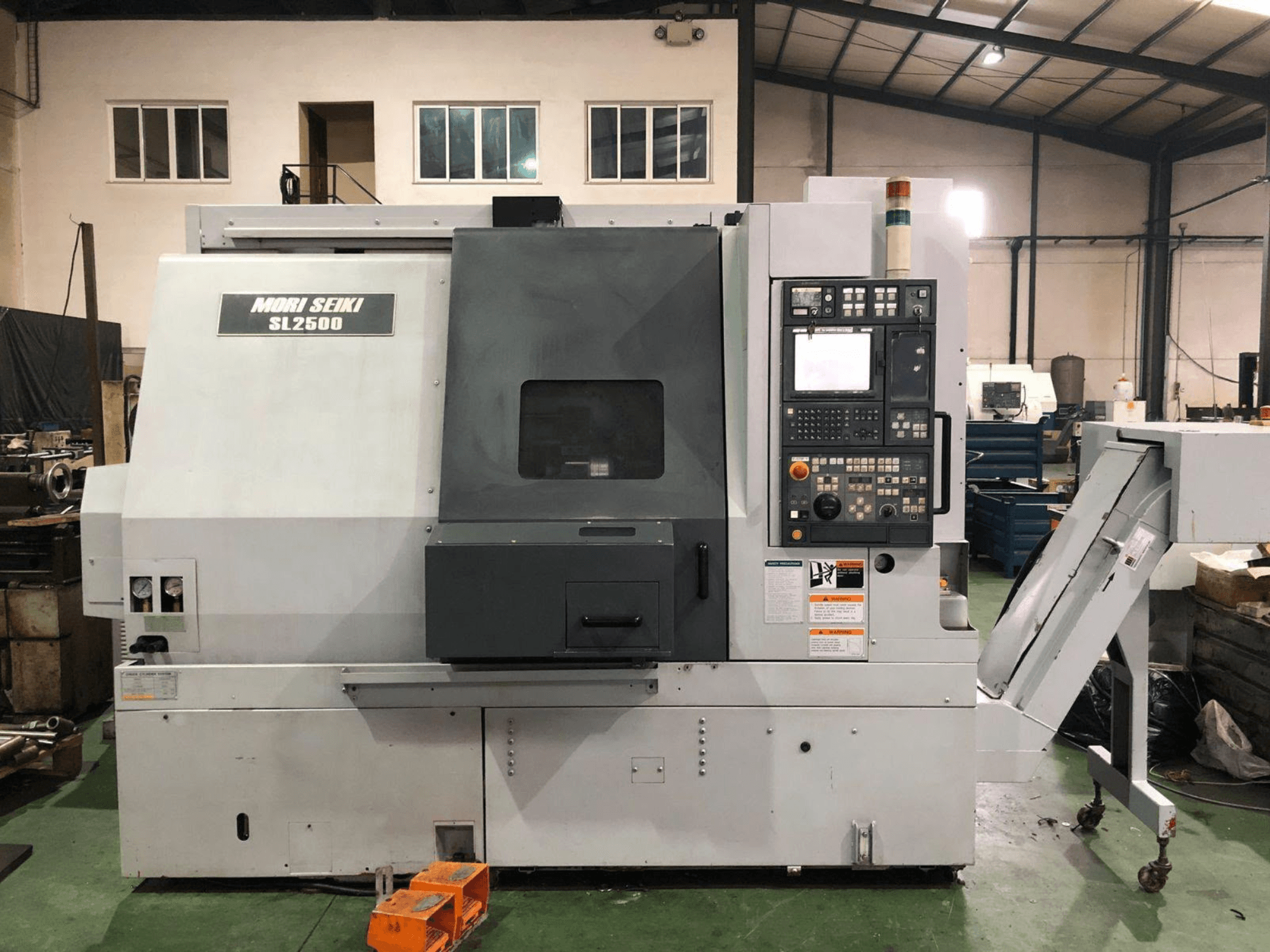 Токарно-фрезерний центр DMG Mori Seiki SL 2500 Y, вид збоку, на якому видно панель управління та конвеєр для відведення стружки.