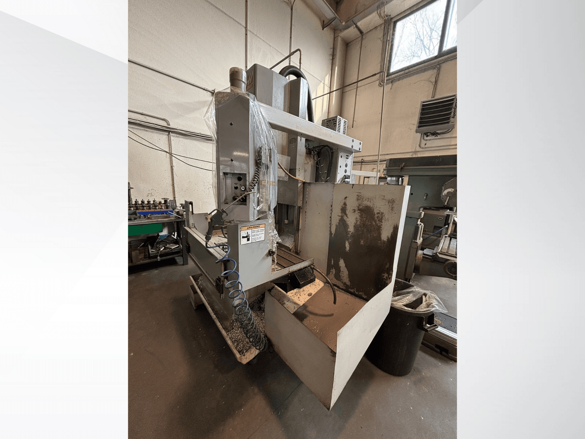 Вертикальний фрезерний верстат із захисним кожухом, вид збоку; видно шланг подачі охолоджувальної рідини та панель керування. Ідеально підходить для обробки.