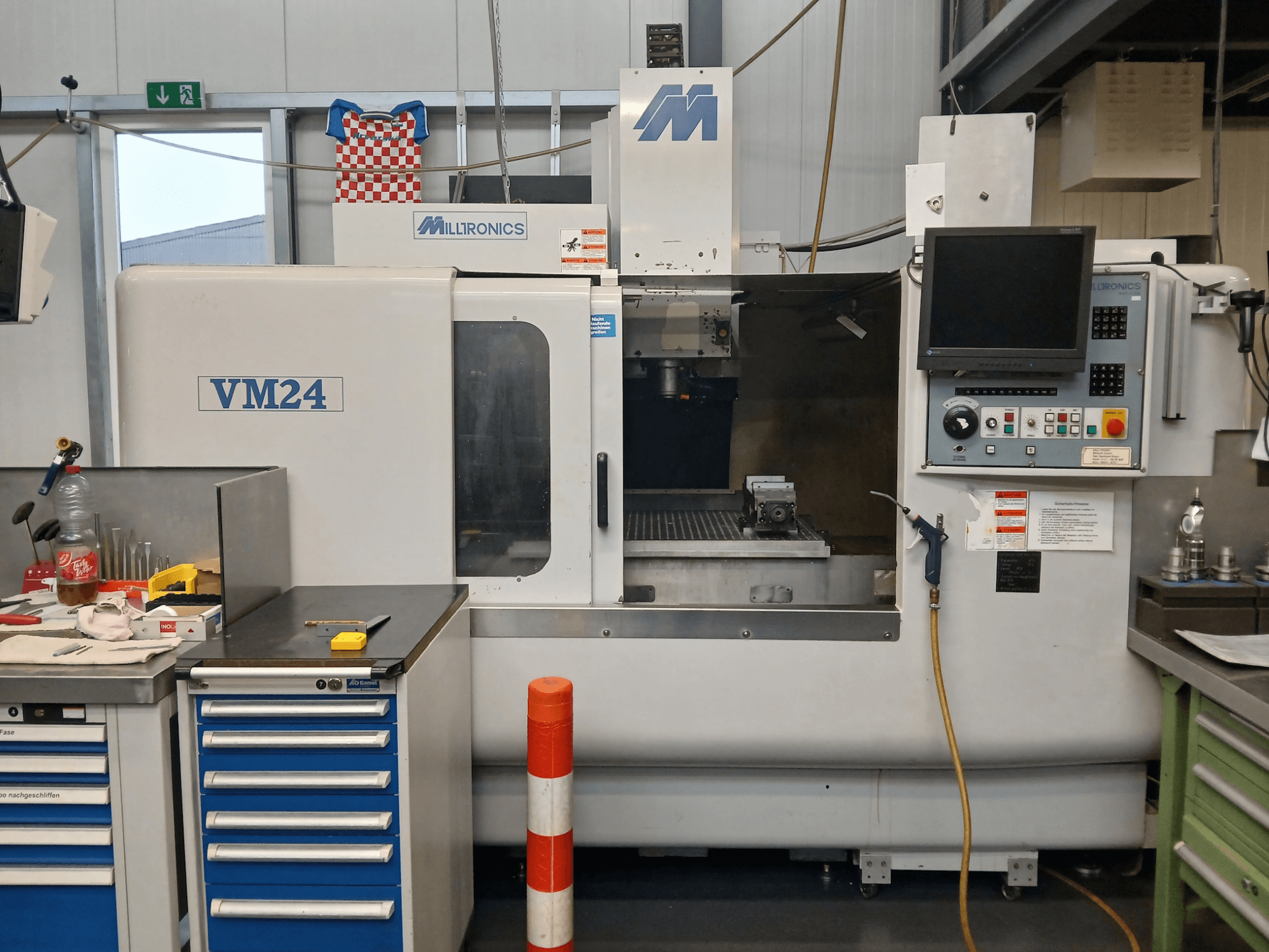 Фрезерний верстат з ЧПК Milltronics VM24 показаний спереду, з панеллю керування, місцем для зберігання інструменту та налаштуванням робочої зони.