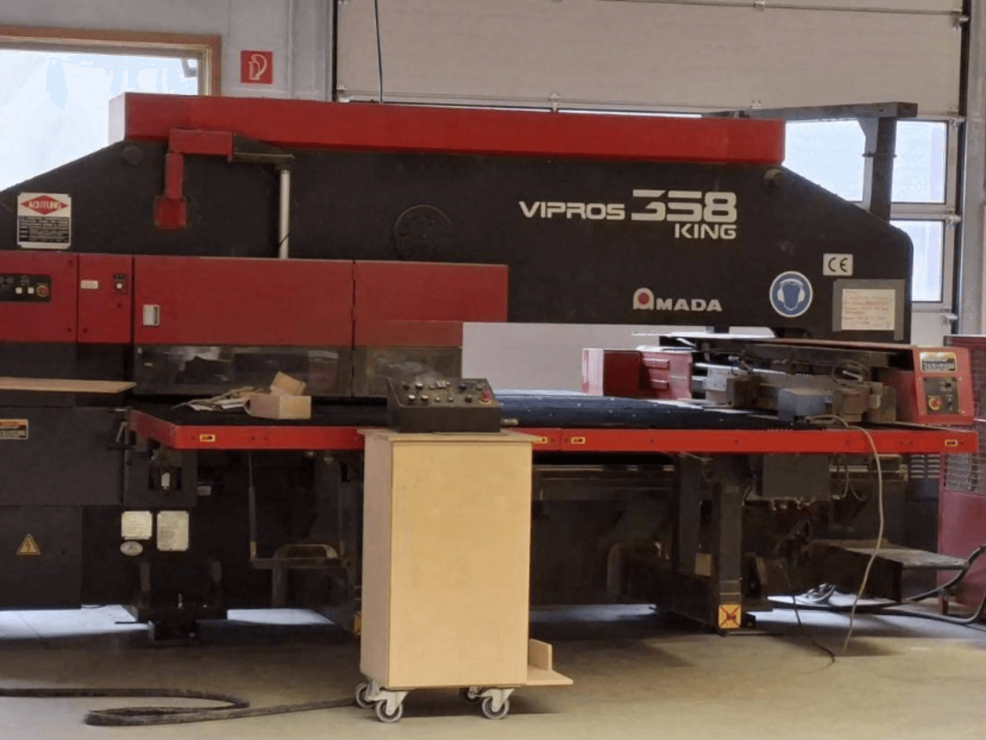Штампувальний прес з ЧПУ AMADA VIPROS 358 KING у боковому ракурсі, на якому видно панель управління та зону зберігання інструментів.