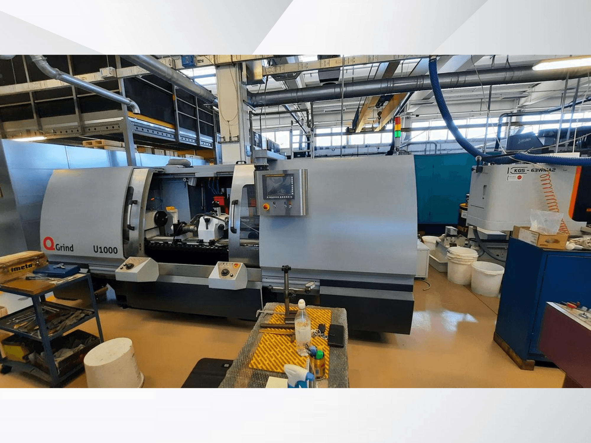 Верстат Q-Grind U1000 в майстерні: вид спереду з панеллю керування та відкритою зоною різання в оточенні обладнання.
