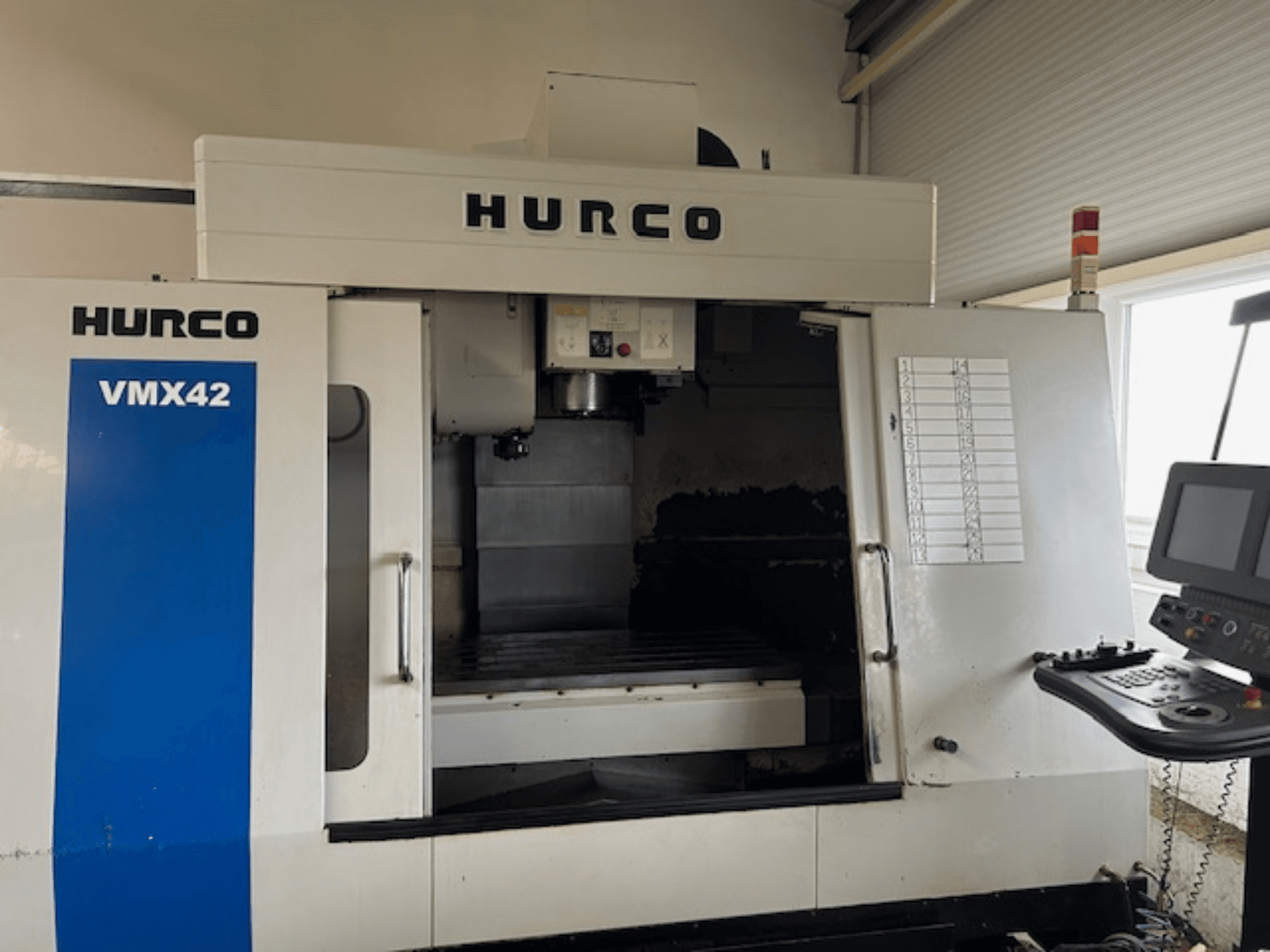 Верстат з ЧПК Hurco VMX42 спереду, з панеллю керування, шпинделем і робочою зоною; показує робочу схему.