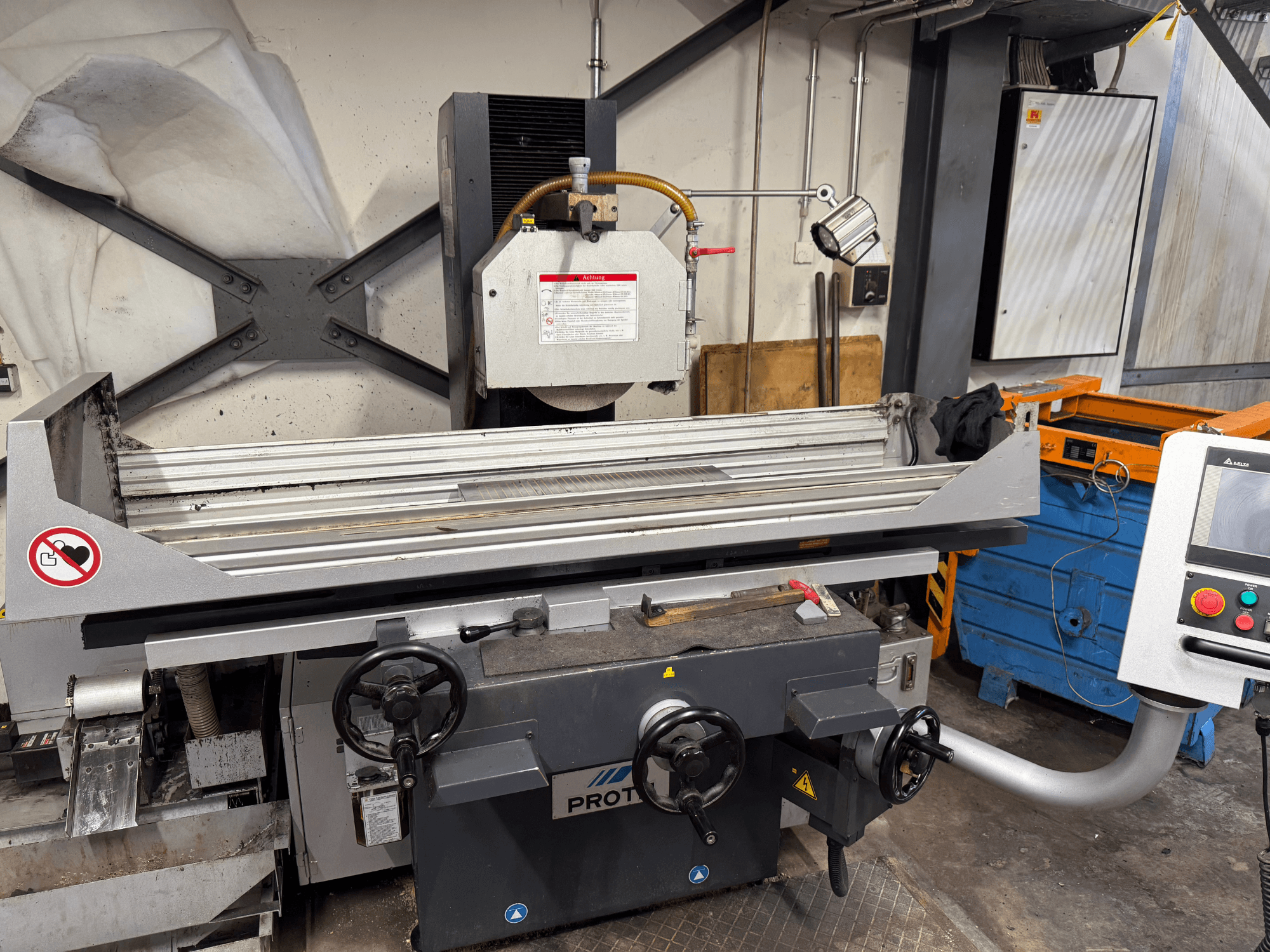 Машина PROTEC, вид спереду, показує плоскошліфувальну машину з ручним керуванням, попередженнями про безпеку та системою охолодження.