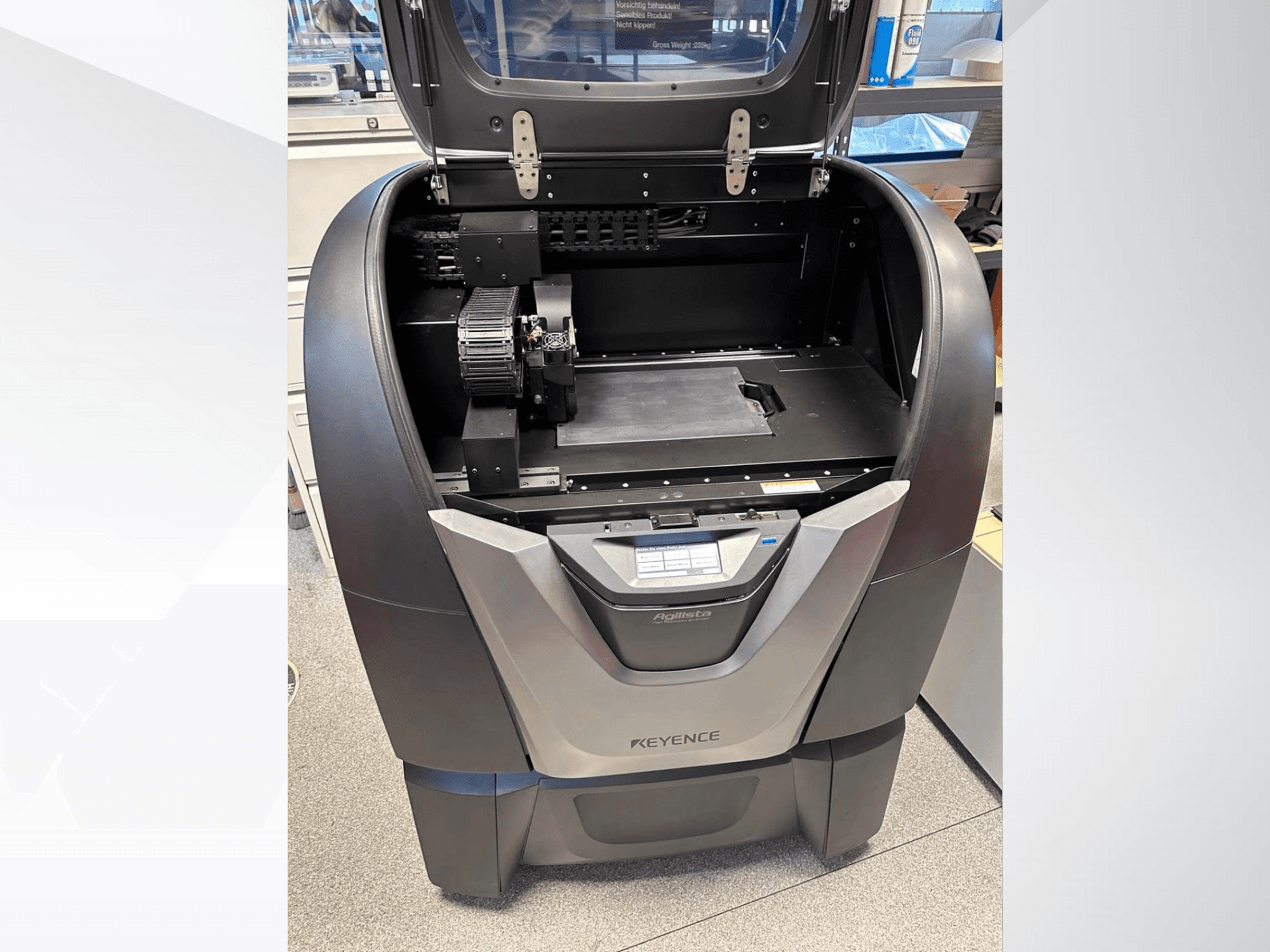 3D-принтер KEYENCE Agilista, вид спереду, демонструє відкритий верх, велику будівельну платформу та внутрішні механічні компоненти.