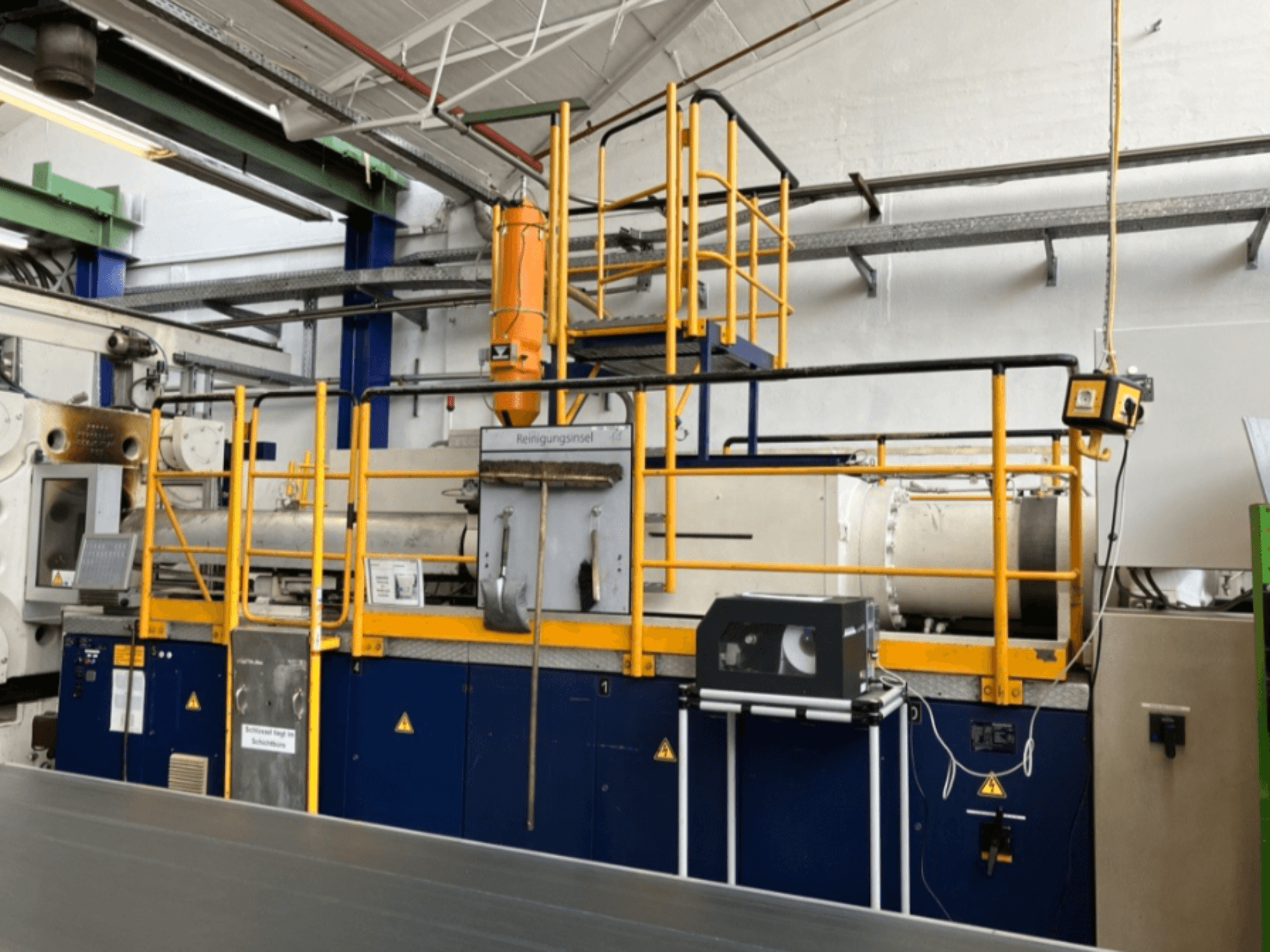 Гідравлічна машина для лиття під тиском Krauss Maffei 1000-8000 M, вид збоку, видно захисну огорожу та панель керування.