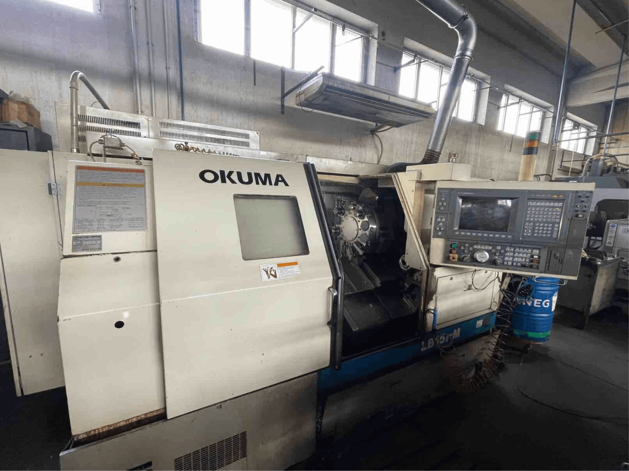 Горизонтальний токарний верстат Okuma LB15i-M, вигляд спереду; панель керування та зона ріжучого інструменту з детальними індикаторами.