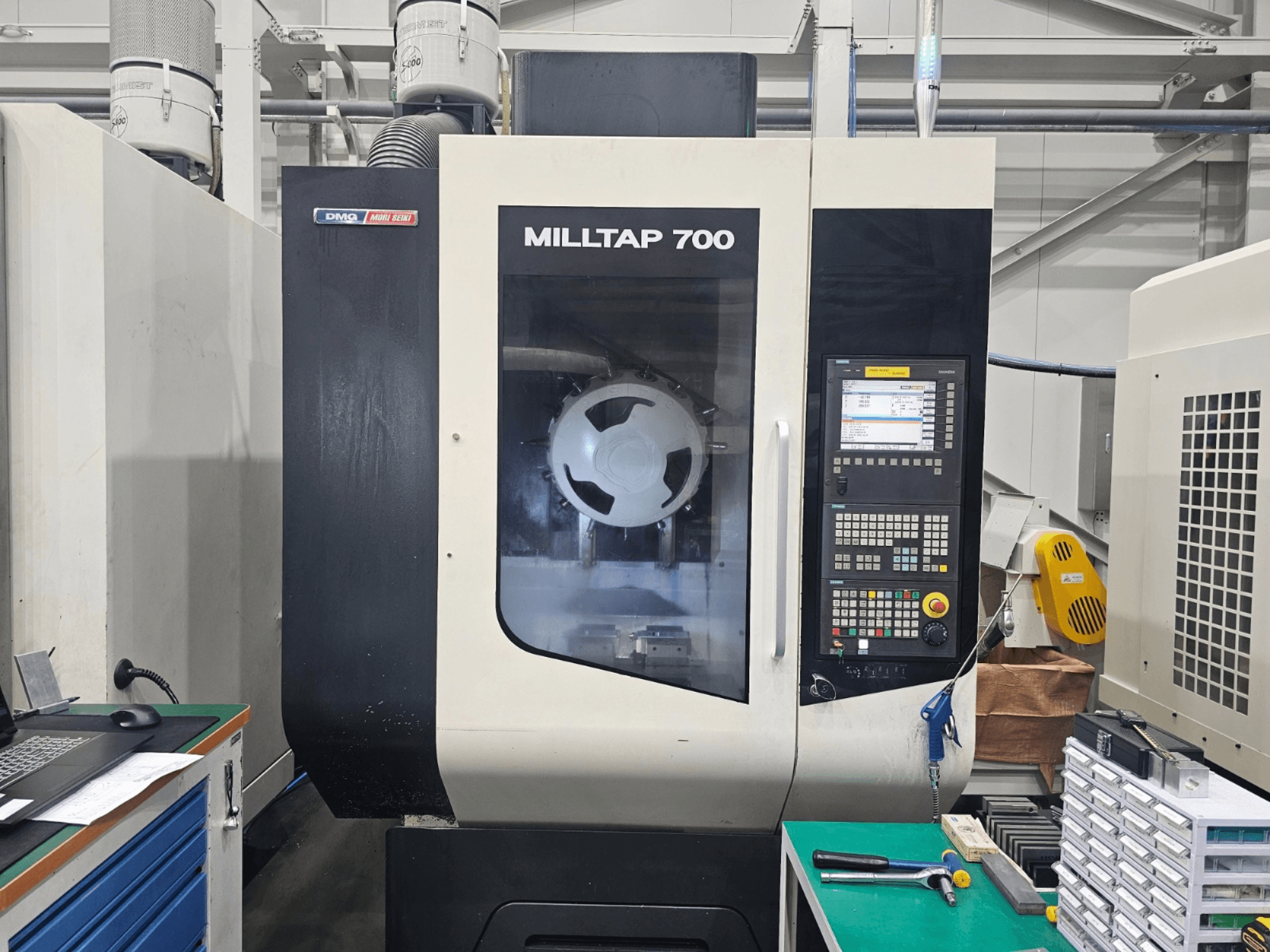 Вертикальний обробний центр DMG MORI MILLTAP 700, вид спереду, на якому видно панель керування, шпиндель та деталі робочої зони.